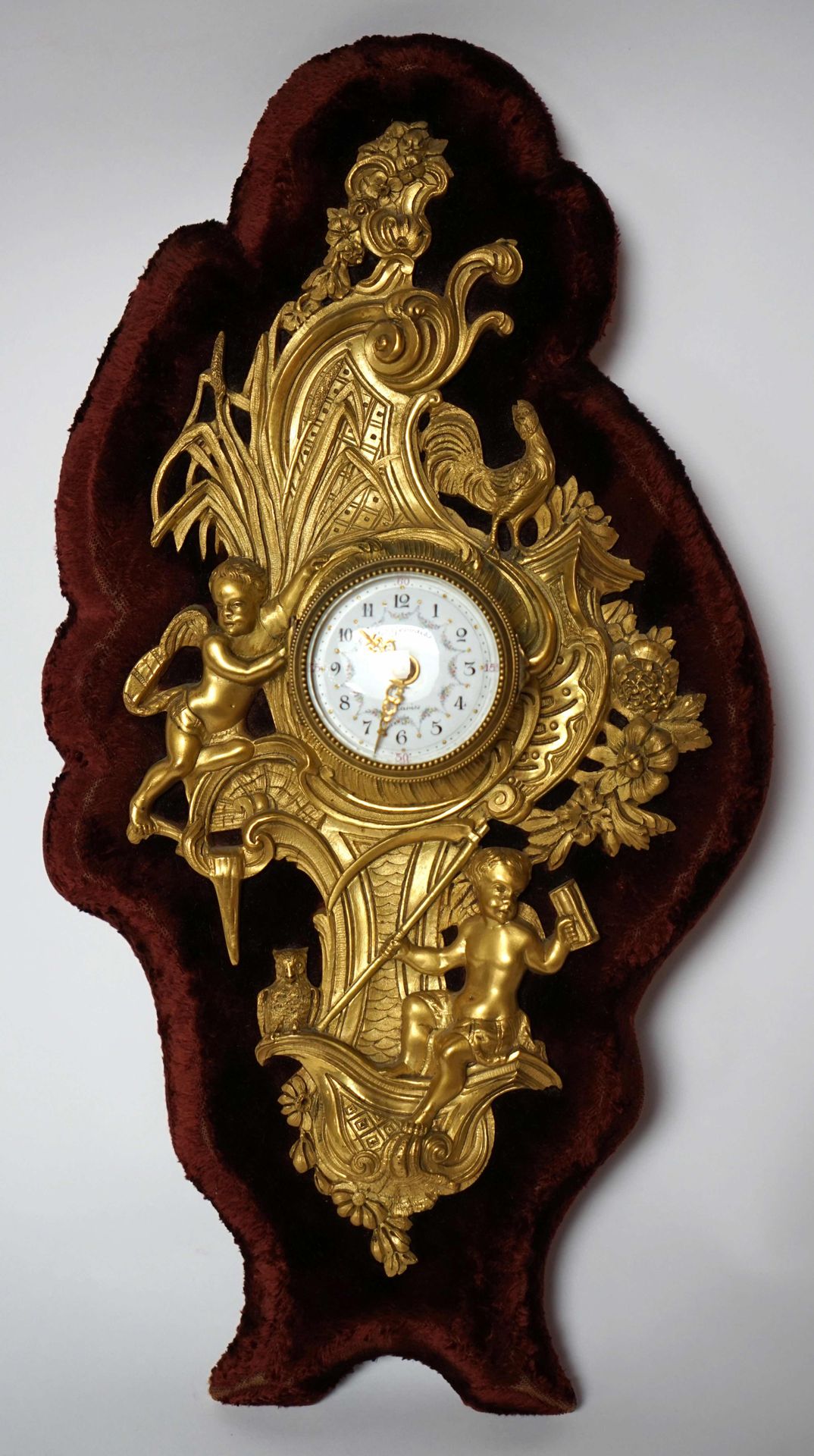 Null 一座木制挂钟，带花环的珐琅表盘上有巴黎Frères Gervais的签名，在紫色天鹅绒支架上装饰着一个Rocaille风格的小天使。总高度为35厘米。
