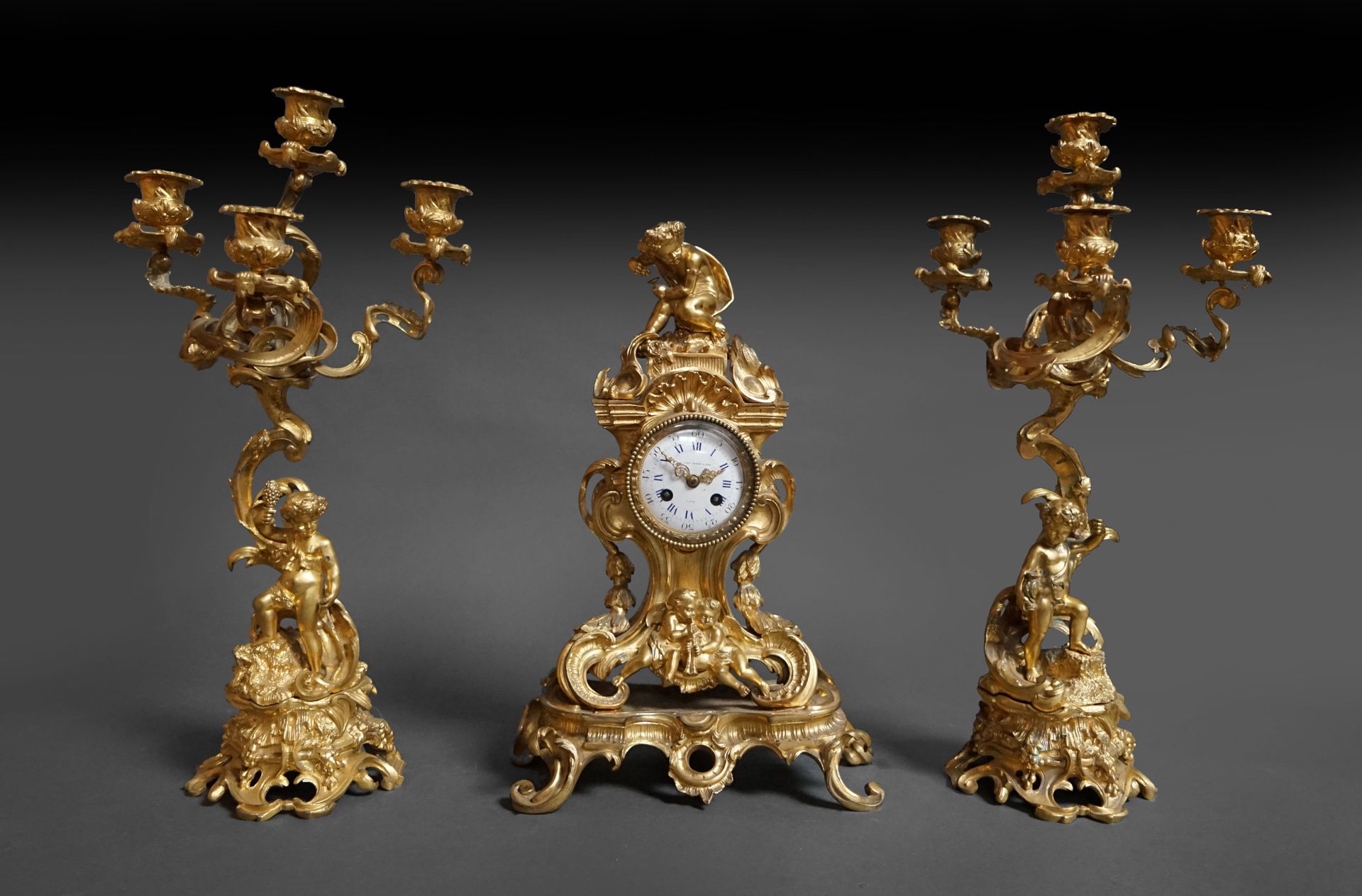 Null 洛可可风格的乌金壁炉，上面有巴克斯头顶的时钟和两个四臂烛台，瓷质表盘上有 "Bigot fils "的签名。拿破仑三世时期。时钟：高 41 厘米，烛台&hellip;