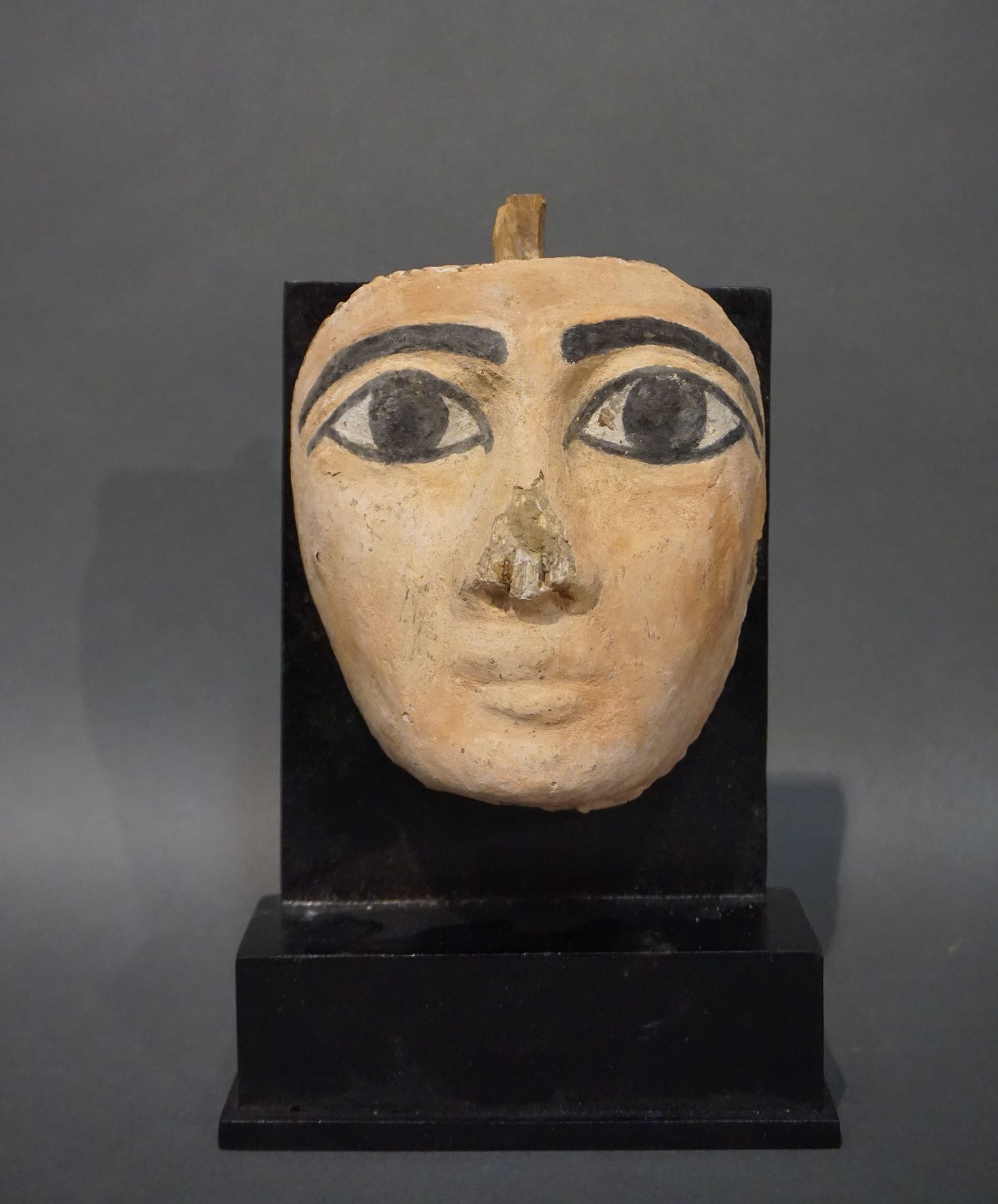 Null 肤色为粉红色的石棺面具。眼睛和眉毛是用黑色勾勒出来的。墙面上的木头和颜料残留。鼻子末端的芯片。埃及，晚期，公元前664-332年 高度：12.5厘米