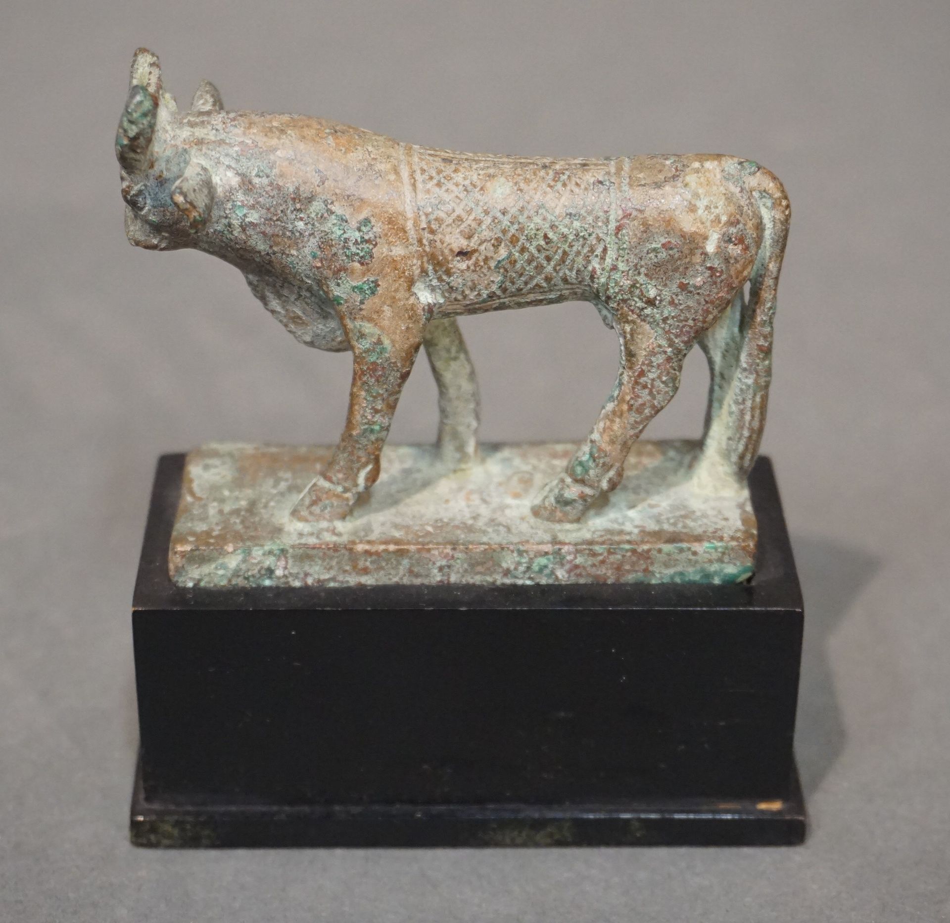 Null 哈托尔牛的塑像。背面刻有方形图案的盖子。青铜，带有光滑的绿色铜锈。缺少太阳盘。埃及，晚期或托勒密时期，公元前664-32年 l. ：7厘米