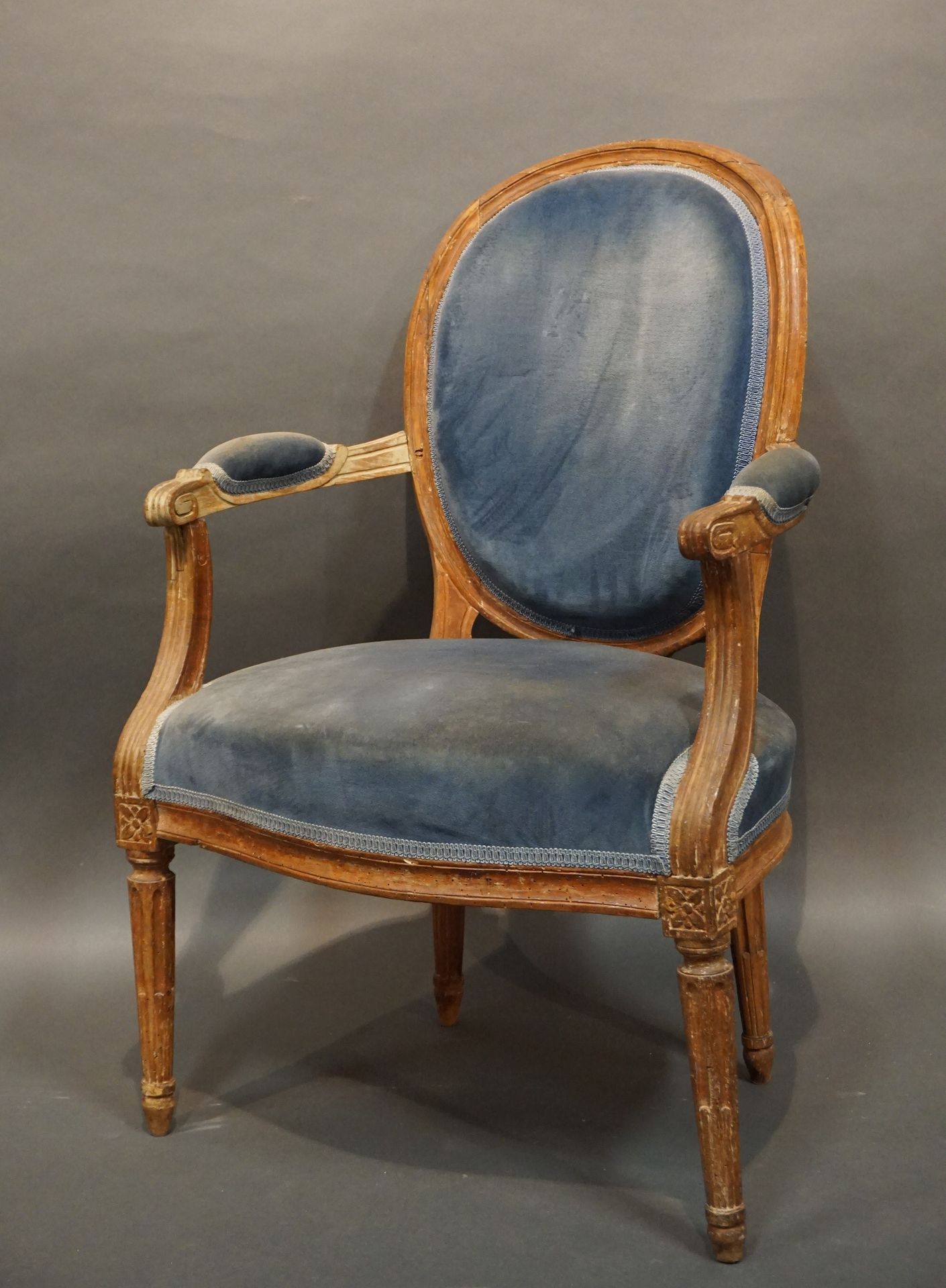 FAUTEUIL 
奖章扶手椅，天然木质，有凹槽和鱼腿，用蓝色天鹅绒做软垫。路易十六时期（磨损）。91x61x60厘米