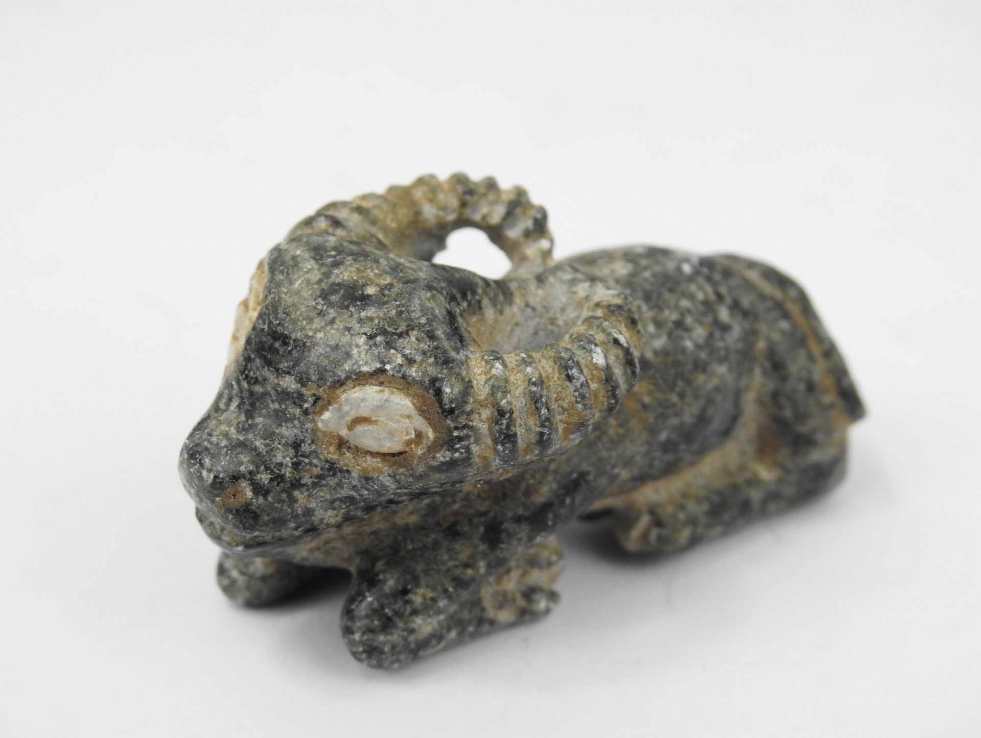 Figurine en pierre sombre d'un animal cornu allongé dont les yeux sont  incrustés de pierre blanche. Dans le style de la Bactriane ancienne. L.   cm.
