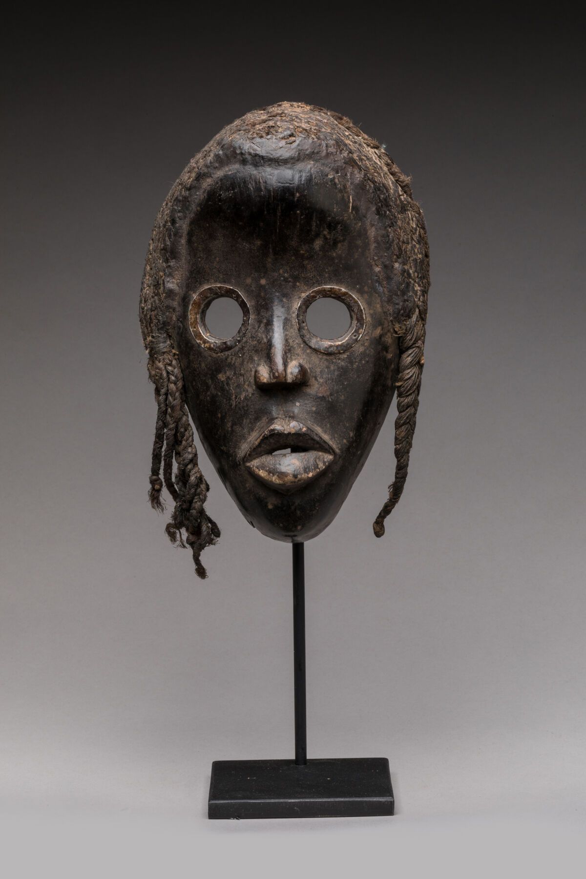Null DAN，象牙海岸。
木头，黑色铜锈。
面具上有一张椭圆形的女性面孔，镂空的眼睛有金属环，头饰由植物纤维制成。
高度：24厘米。宽度：15.5厘米。
小&hellip;
