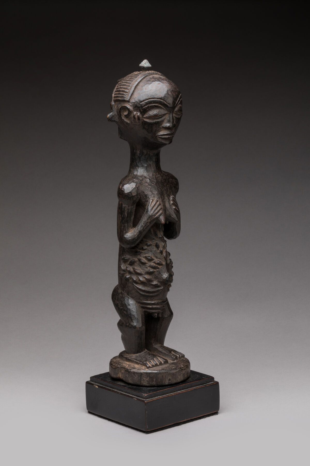 Null LUBA，刚果民主共和国。
硬木，深色，略带油性的铜锈，有光泽的反射。
站在圆形底座上的女性雕像，双手放在乳房上，面容安详，腹部有丰富的瘢痕装饰 
女&hellip;