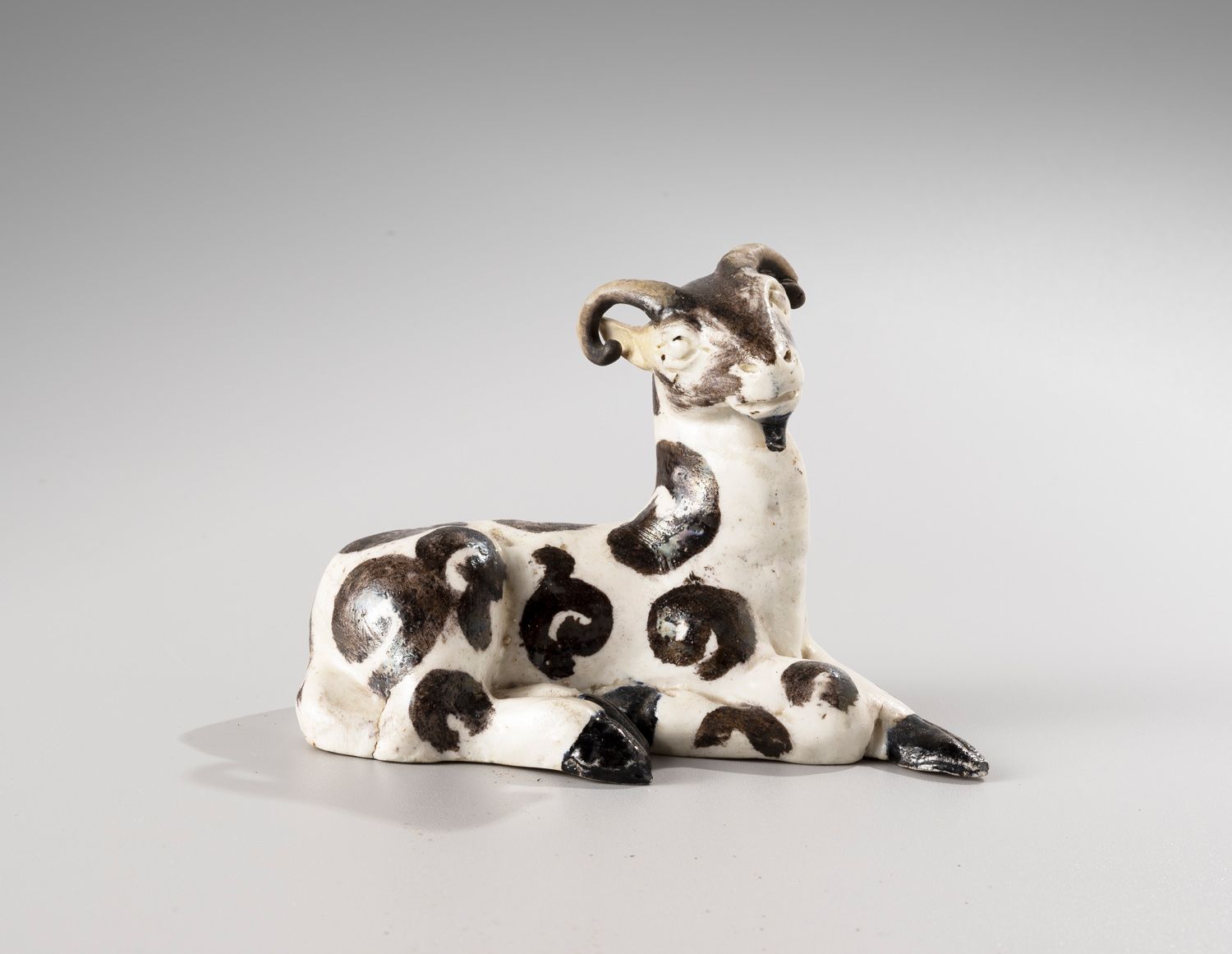 Null 中国，18世纪

白色和黑色的珐琅彩瓷器主题，代表着

一只躺着的山羊，一条腿折叠着。

长13.5厘米-高10厘米

(一个耳朵和右角的修复，小裂缝&hellip;