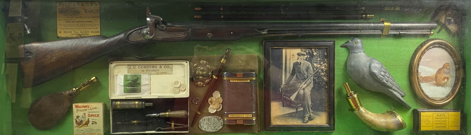 Null 猎人的纪念品在玻璃下的框架中，包括一支打击步枪，火药瓶，一个相框，一个代表鹧鸪的小椭圆形画，一个狐狸头，小工具等。

42 x 124厘米