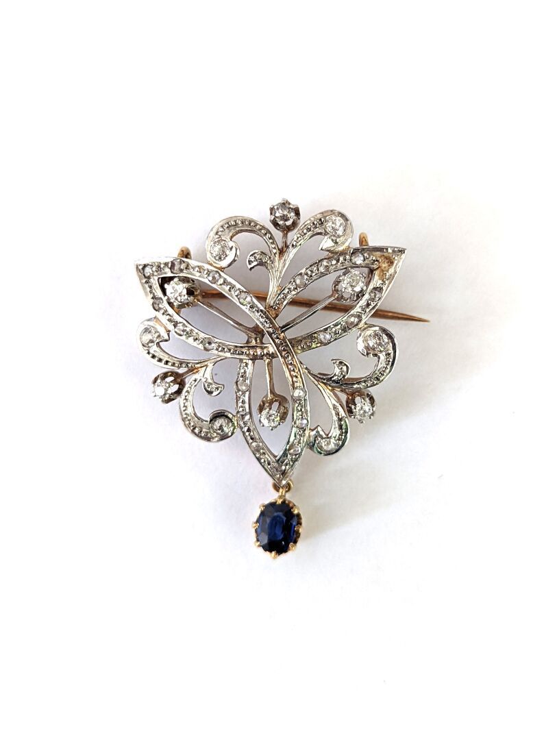 Null 双色(750)18K金胸针，形成镶嵌着玫瑰式切割钻石的阿拉伯式图案。一块仿制的蓝色石头作为吊坠。19世纪晚期。

重量 : 10,70 g

马