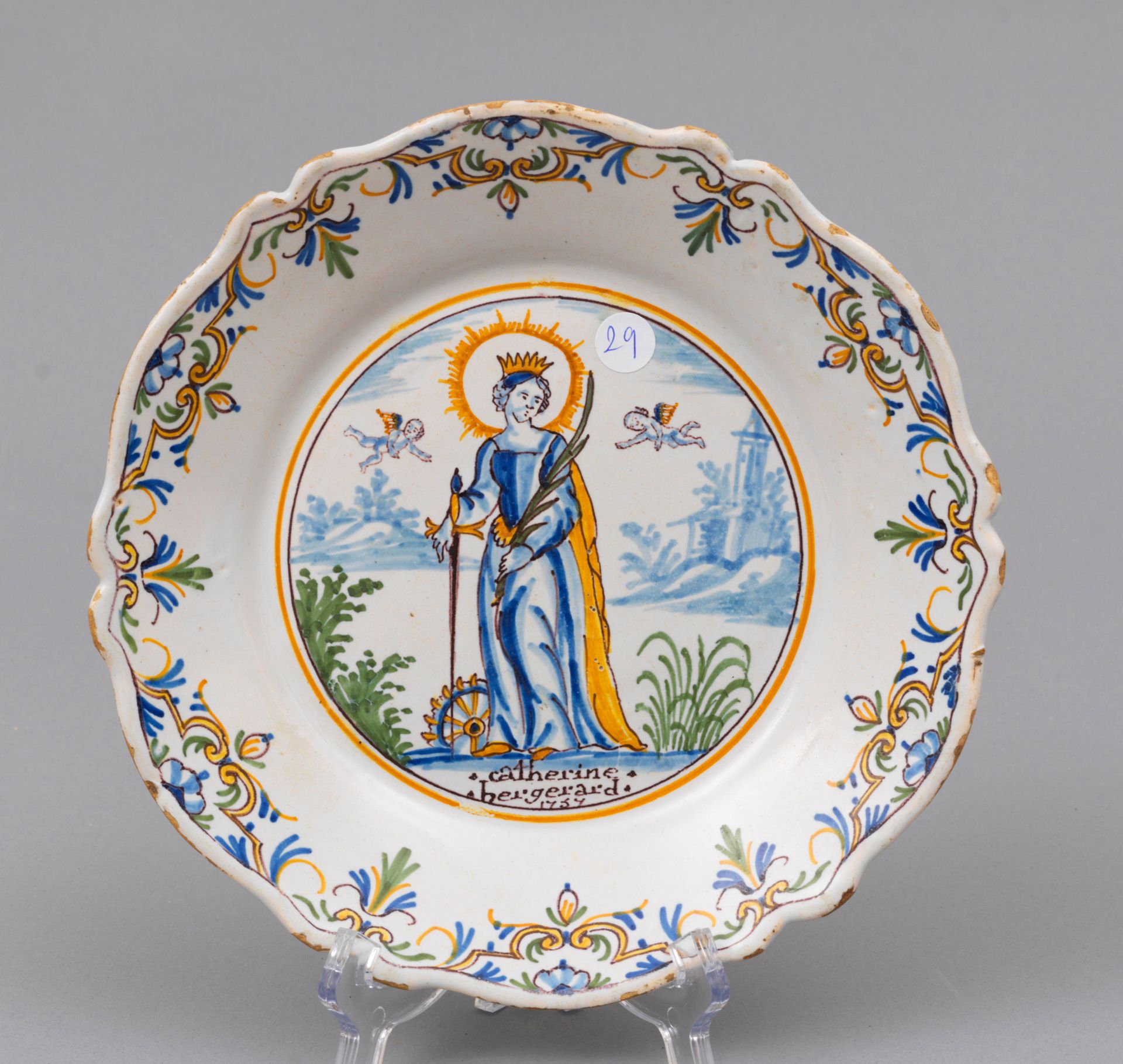 Faience Nevers 
内韦尔

陶器盘子，边缘有轮廓，中间有多色装饰，是一个站立的圣凯瑟琳的徽章，周围有两个小天使和一个小男孩。

底部刻有".Cat&hellip;