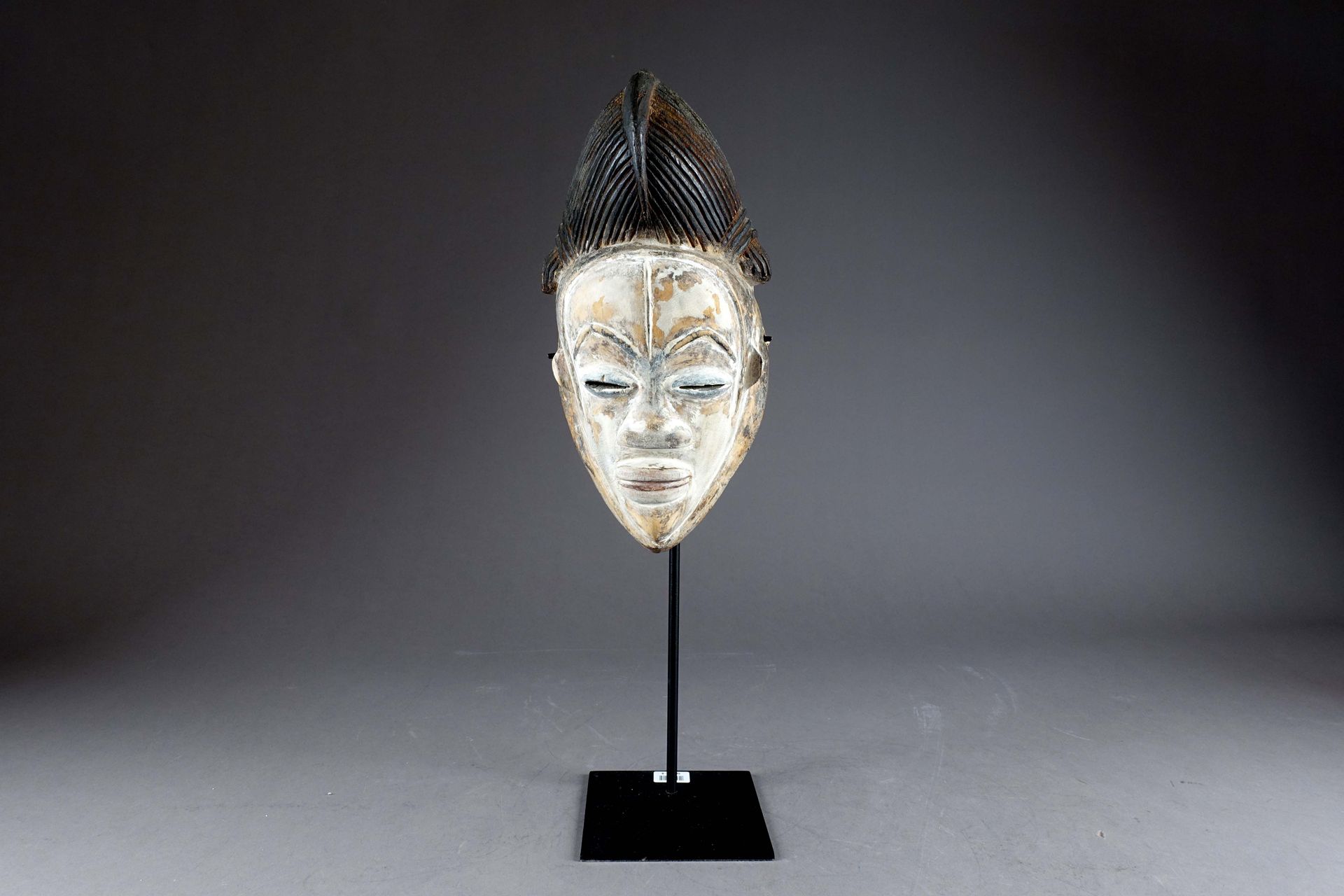 Masque Punu. 杏仁型脸，梳着有造型的辫子的发髻。雕刻的木头带有铜锈，部分被高岭土覆盖。加蓬。高度：33厘米。背面有一个标签：Collection L&hellip;