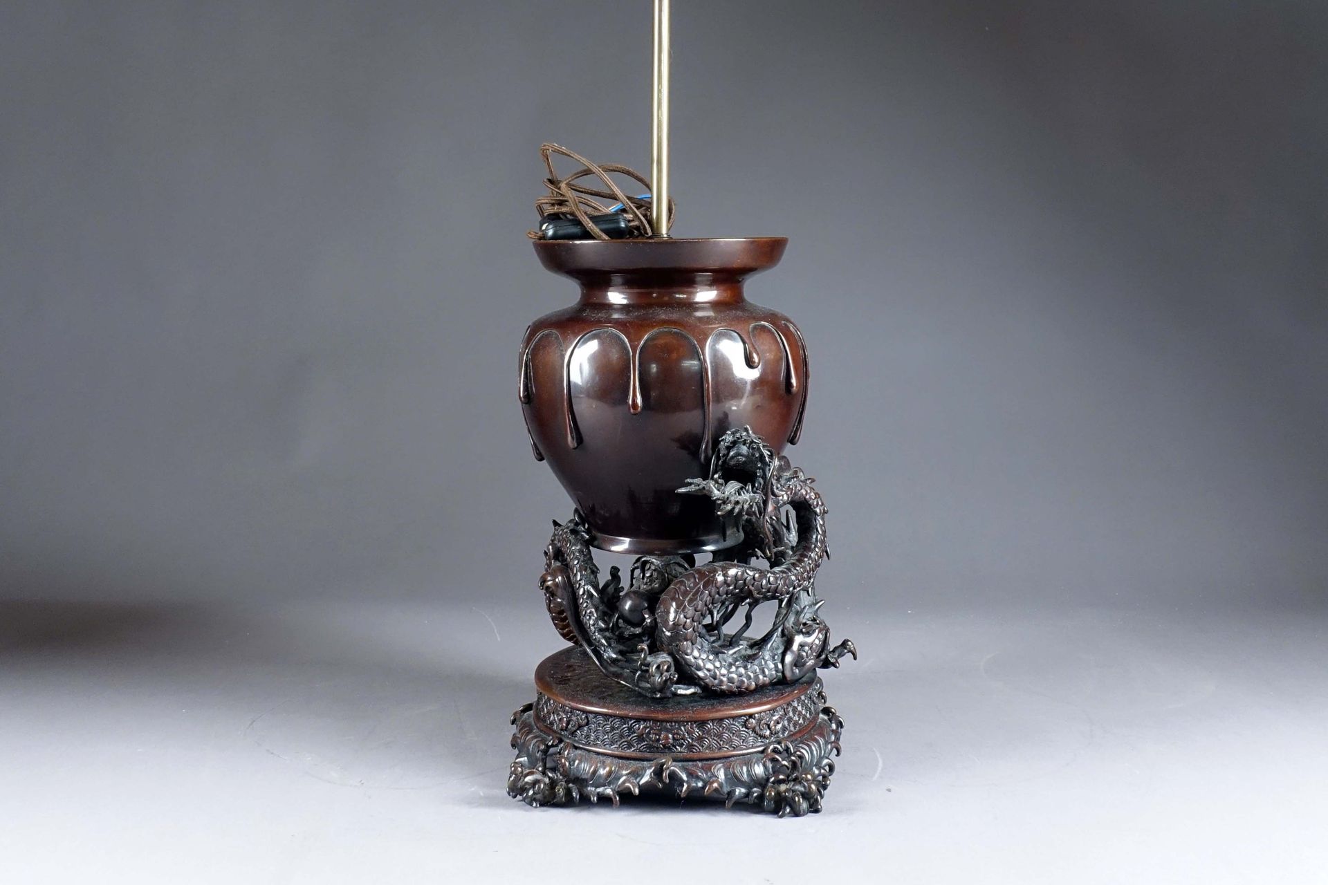 Japon - Période Meiji. 花瓶由一条盘在自己身上的龙携带，站在有波浪图案的露台上。青铜，带有棕色的铜锈。安装成一盏灯。花瓶的高度：37厘米。&hellip;