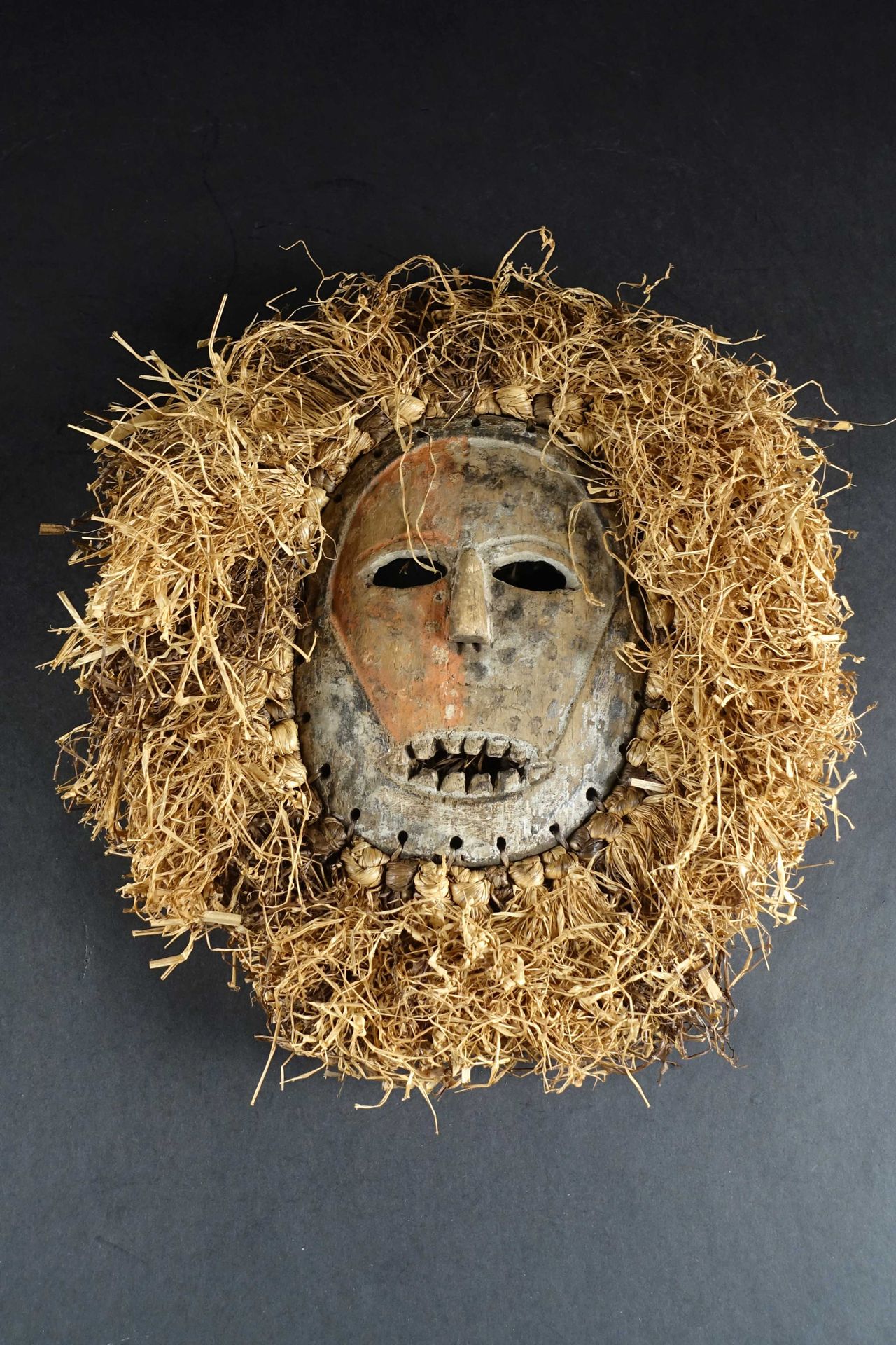 Masque Ndaaka en bois tendre. 有一张部分图式化的椭圆形脸，覆盖着红色的颜料，周围有一个酒椰叶的头饰。刚果民主共和国。高度：44厘米&hellip;