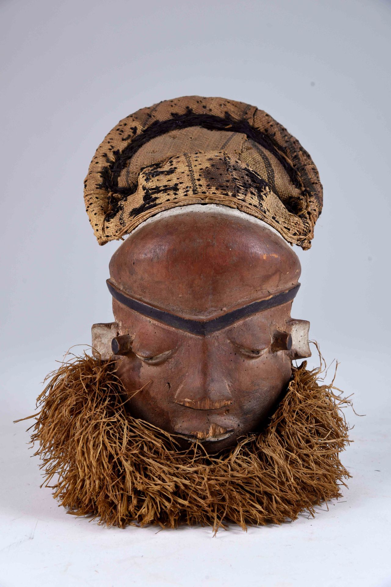 Culture Pende. Maschera Mbuya con volto triangolare, palpebre pesanti e mento ci&hellip;