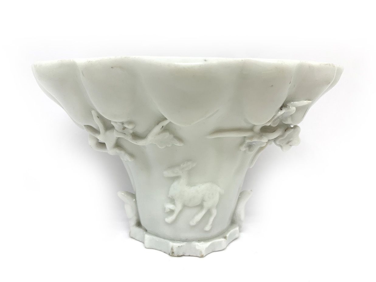 CHINE (Dehua) 仿犀牛角的白釉瓷酒杯，微微浮雕着山、梅花、鹿、龙头和奇美拉
18世纪
高：8.5厘米
 （有些缺口