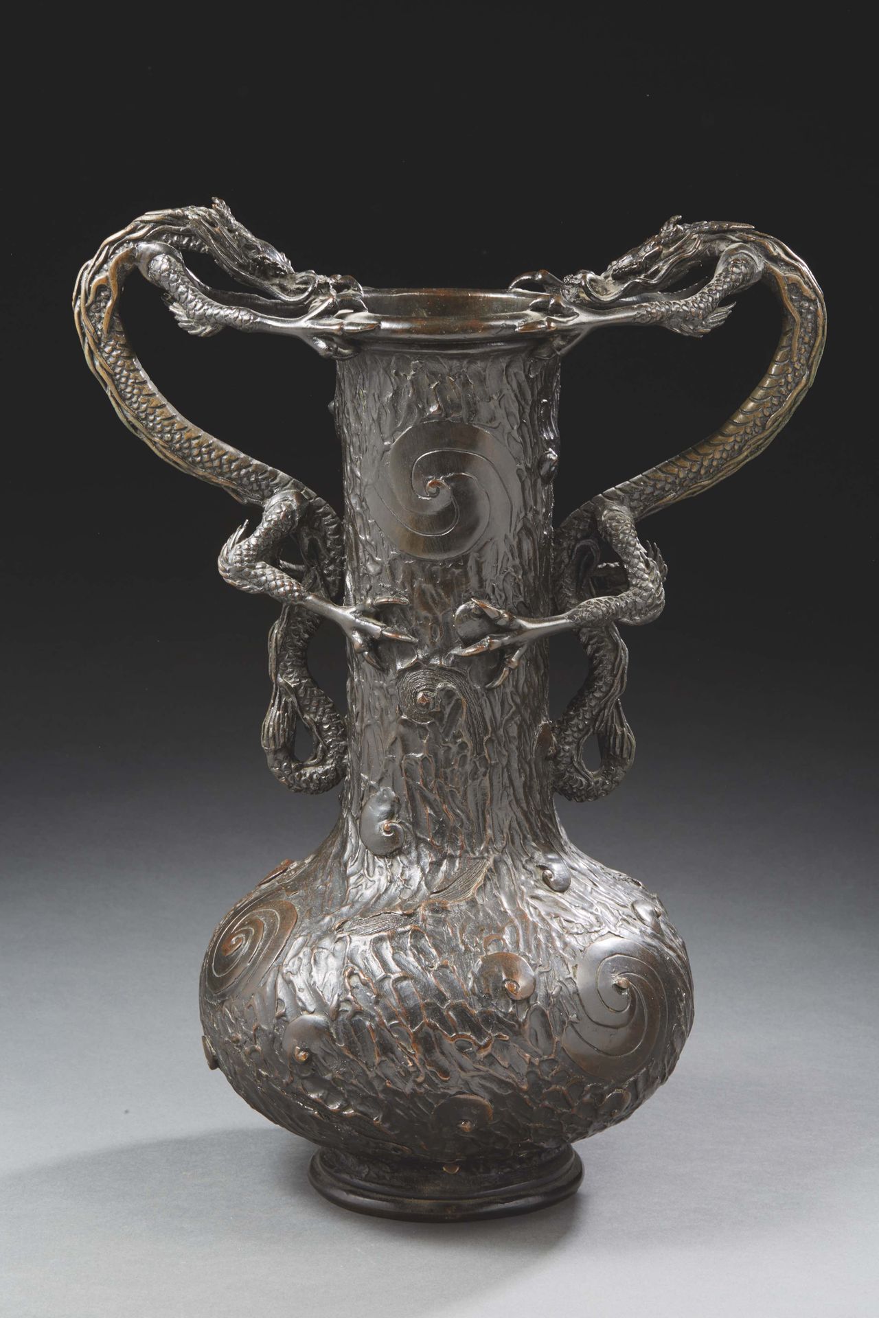 Null 日本 - 20世纪初


一个大的低体花瓶，窄颈，两个龙形把手，铜制，有棕色的铜锈，在树皮状的背景上装饰着螺旋形。高47厘米。