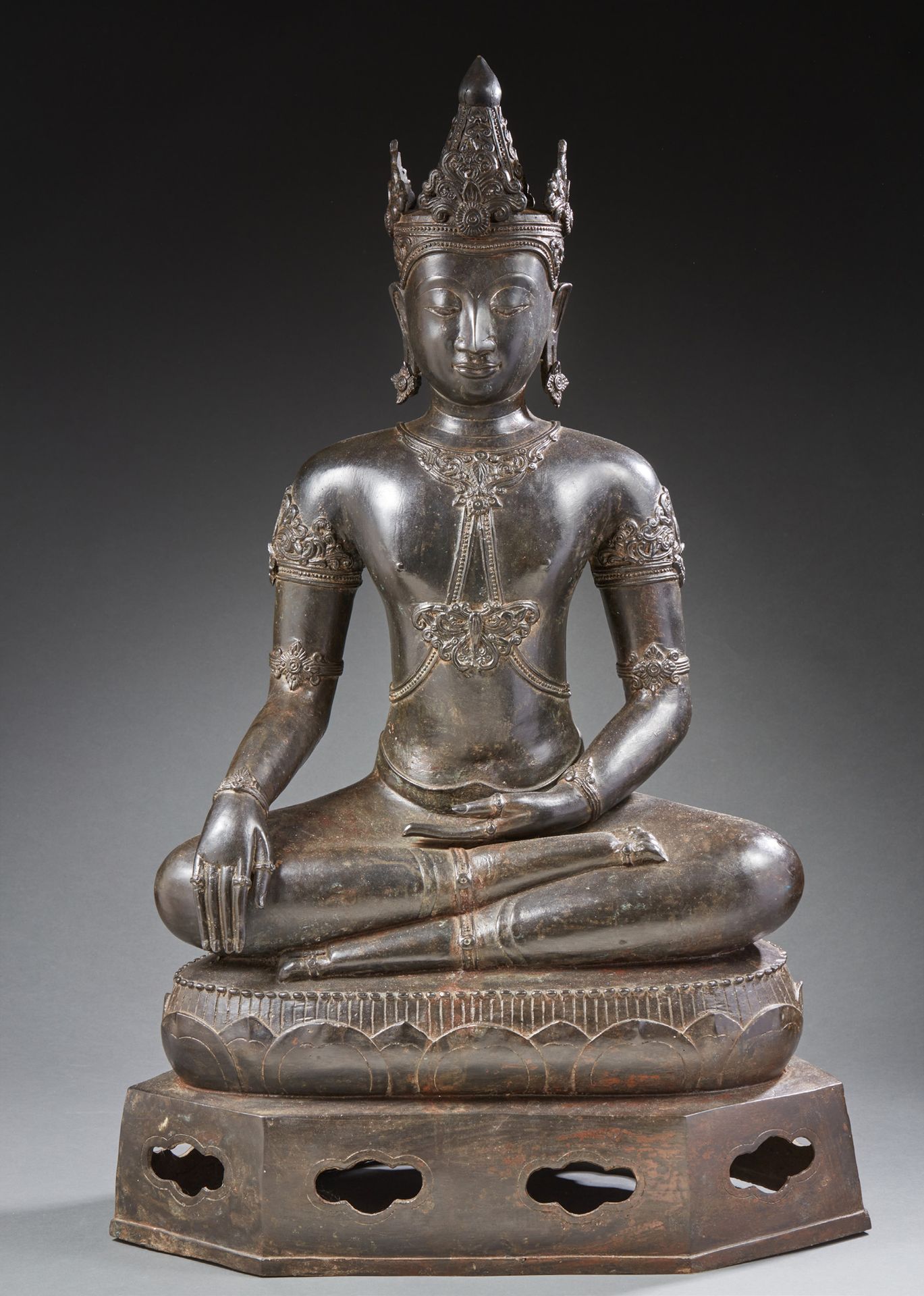 ASIE DU SUD-EST (THAÏLANDE) 一尊大型棕色铜质释迦牟尼佛坐在莲花状的基座上，基座上有一个六角形的镂空底座。他戴着一套丰富的珠宝胸饰，手&hellip;