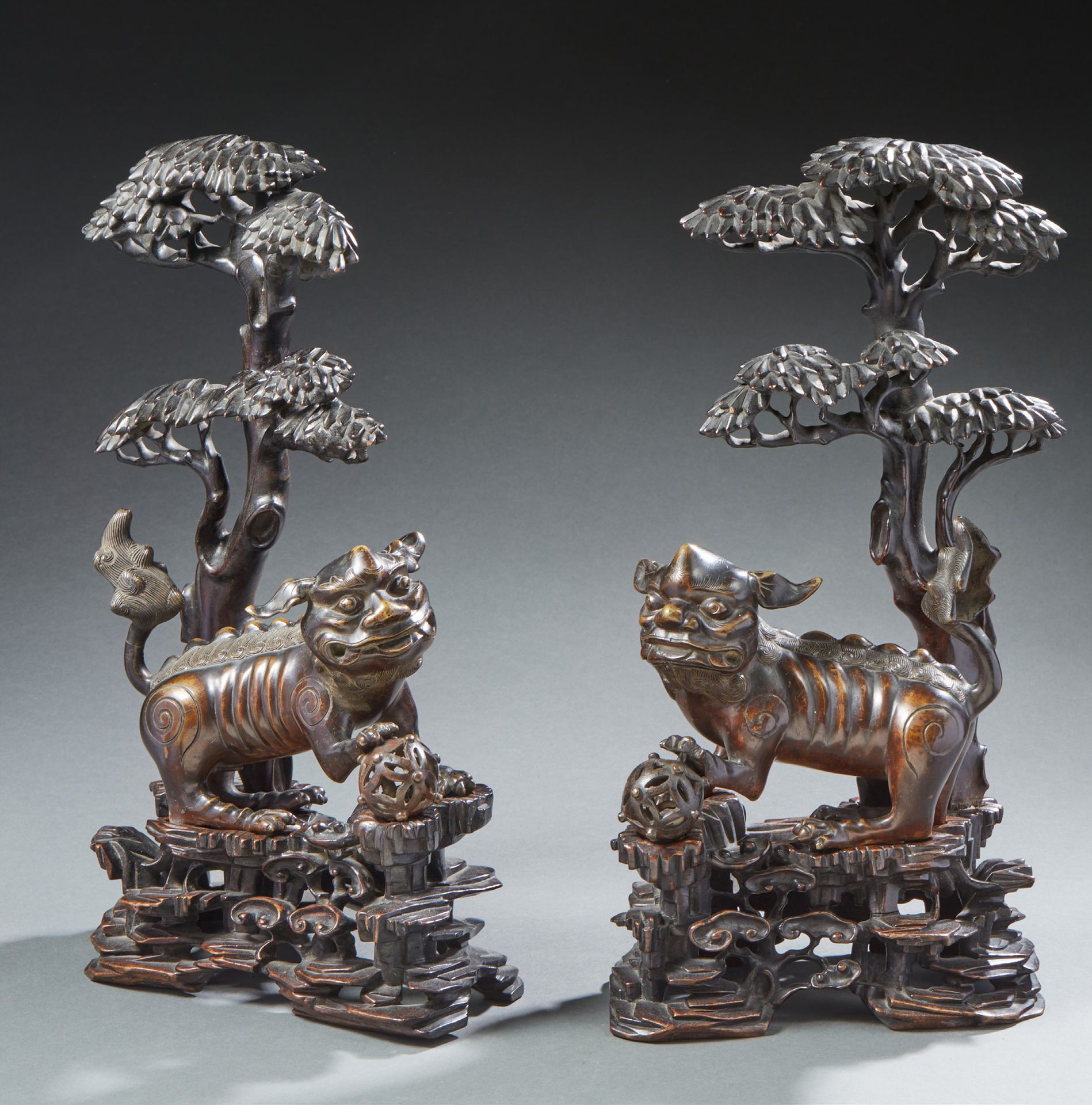 CHINE 一对青铜棕色的佛教狮子，坐着，其中一只脚放在一个镂空的球体上。它们矗立在镂空的木质底座上，石头上长着灵芝蘑菇，伞形松树从里面冒出来。19世纪的H.4&hellip;