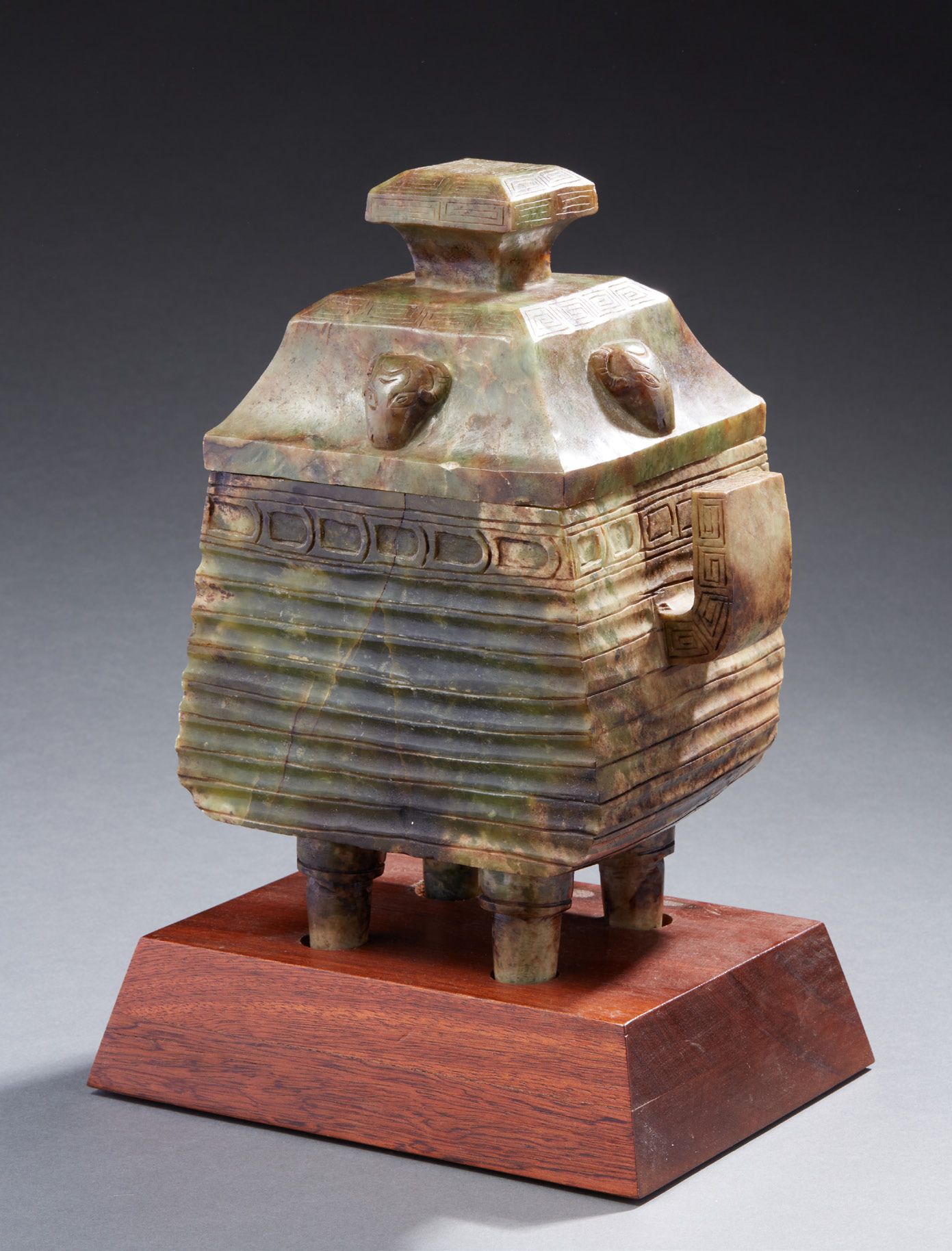 CHINE 古代雕刻的四角形玉瓶，立于四条腿上，背景为灰绿色，有许多棕色的铁锈痕迹，盖子上有四个公羊头，瓶身有凹槽 现代时期 木质底座 高：28厘米