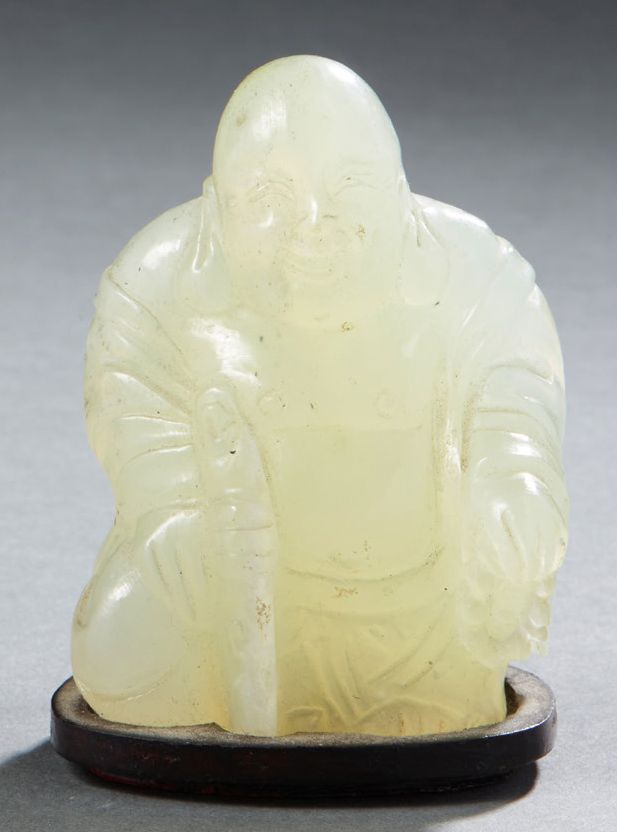 CHINE Carved light jade figurine of a seated Buddha holding a stick in one hand &hellip;