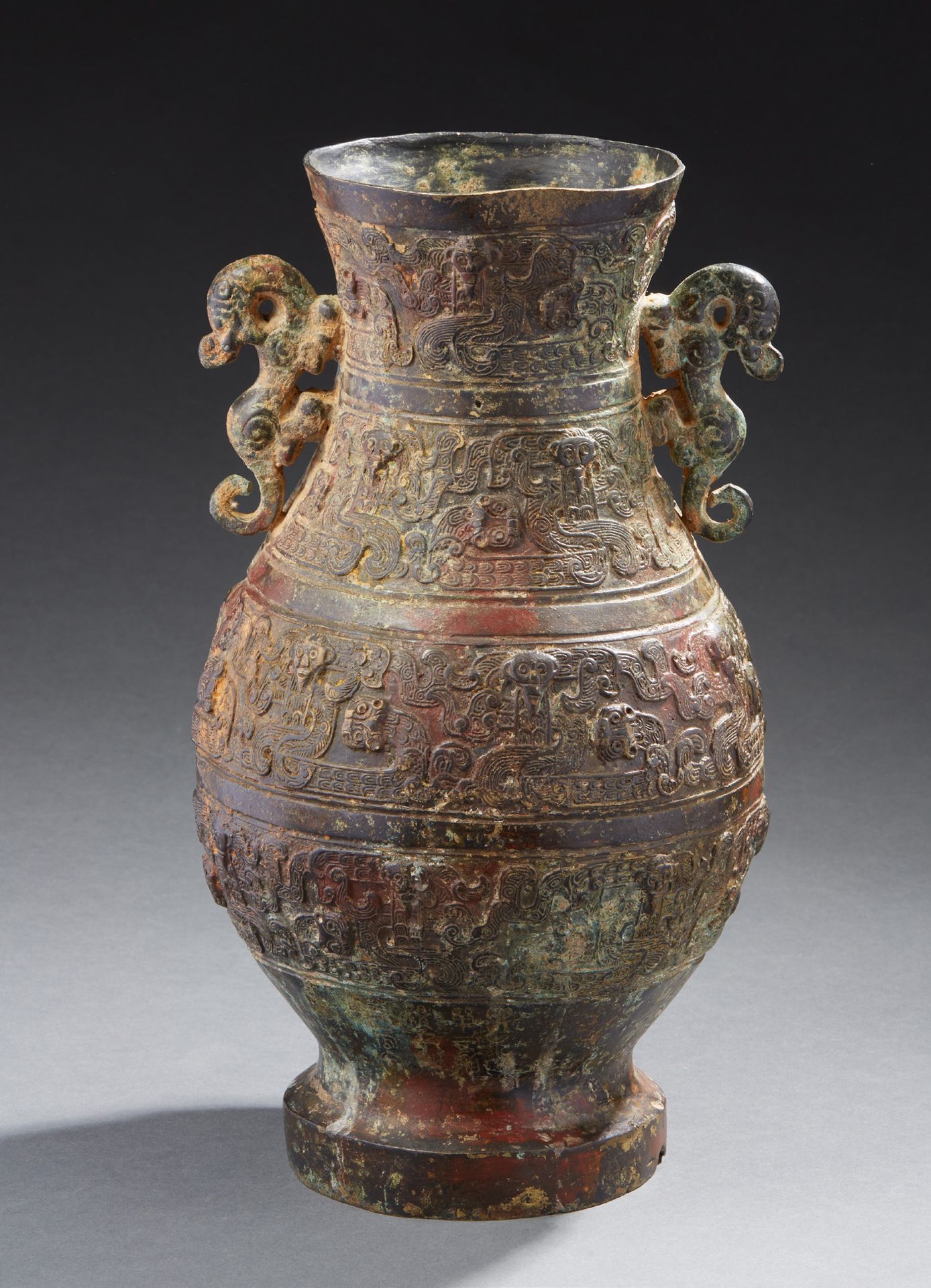 CHINE 一个有红棕色和绿色铜锈的青铜花瓶，微微浮雕着饕餮面具和嵌合体，镂空的把手描绘着窑洞。底部有风格化的铭文 古代风格的作品 底部有一小块缺失，一块被粘回&hellip;