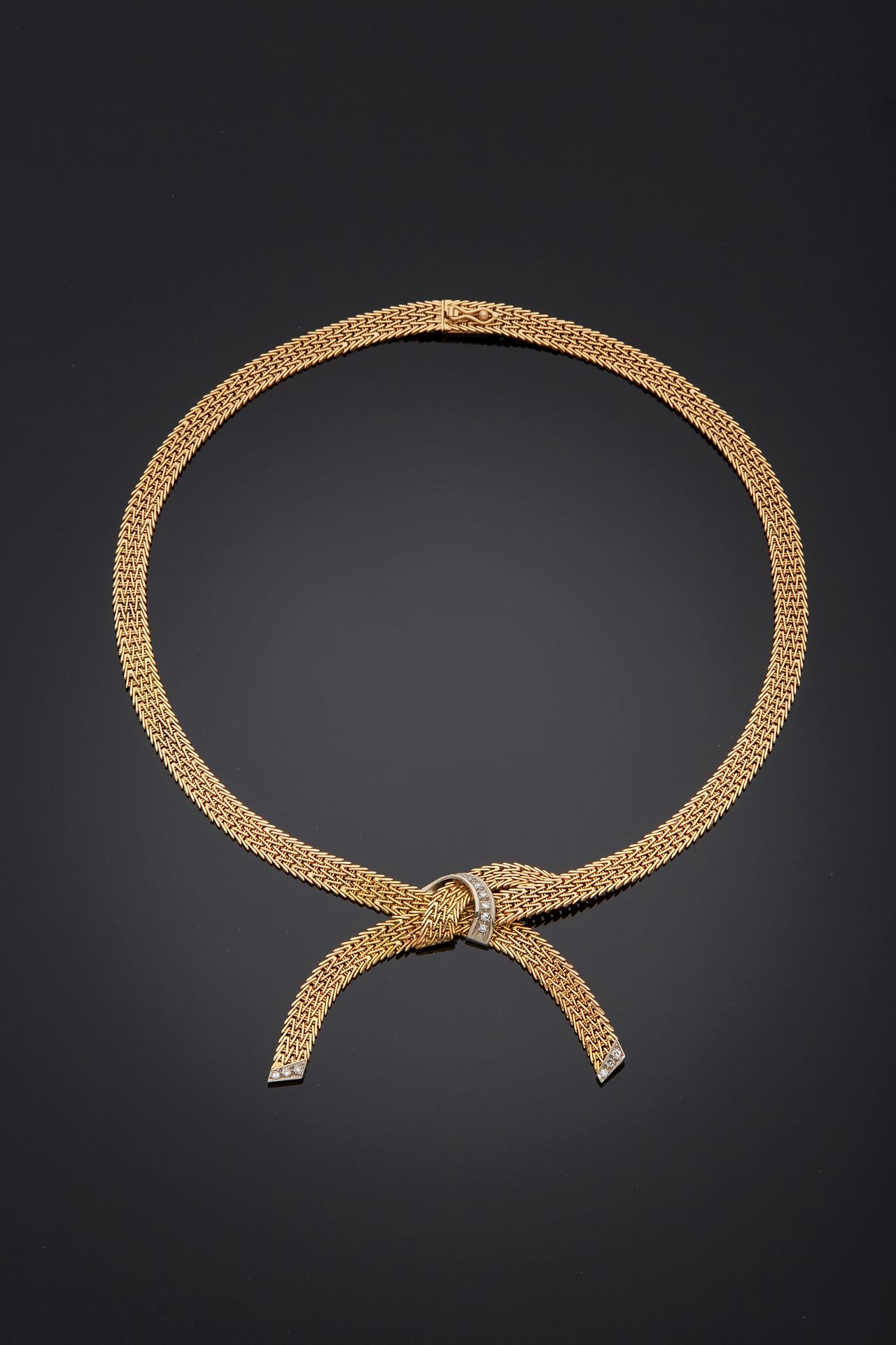 Null 一条750毫米的黄金项链，有一个平坦的铰链，形成一个交叉结的图案，并由一个镶嵌有八分之一钻石的链接加强。
约1960年的法国作品。
长度：42厘米
毛&hellip;