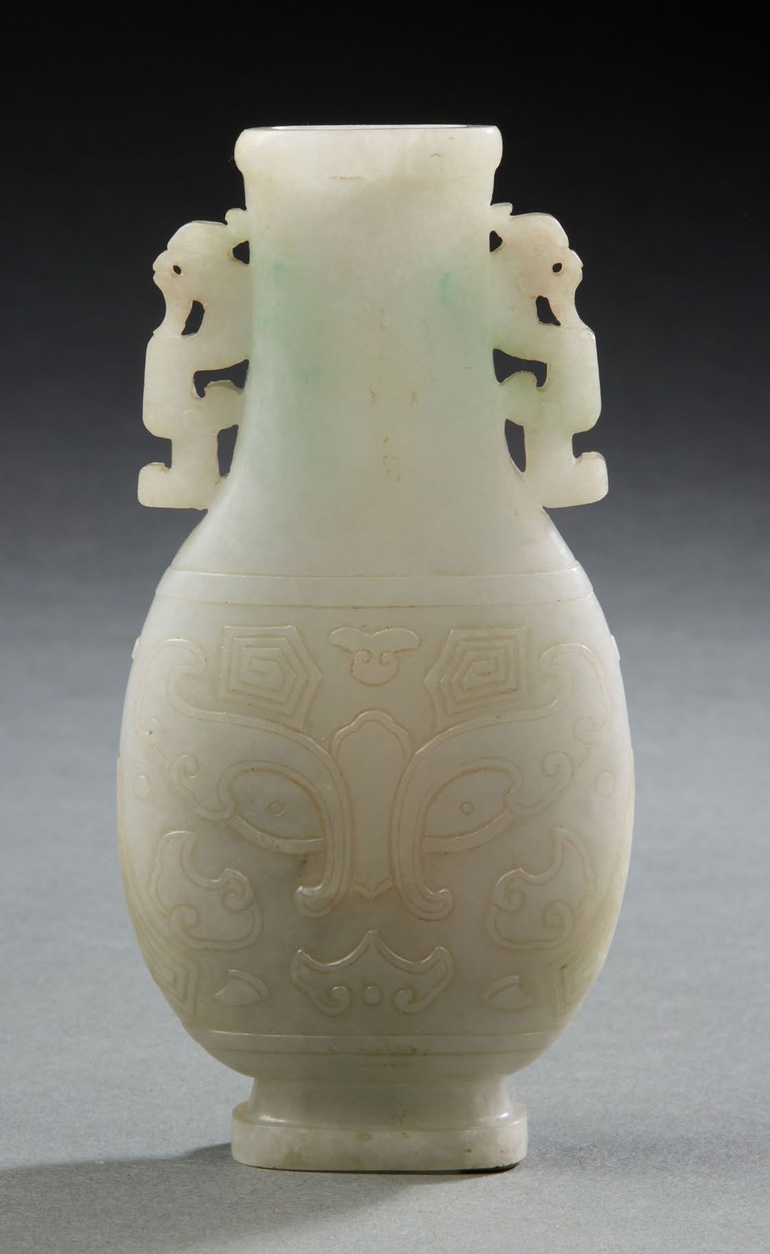 CHINE, vers 1900 一件略带绿色浸润的翡翠柱形花瓶，有两面饕餮面具装饰。颈部饰有两条风格化的龙。
H.12,5 cm