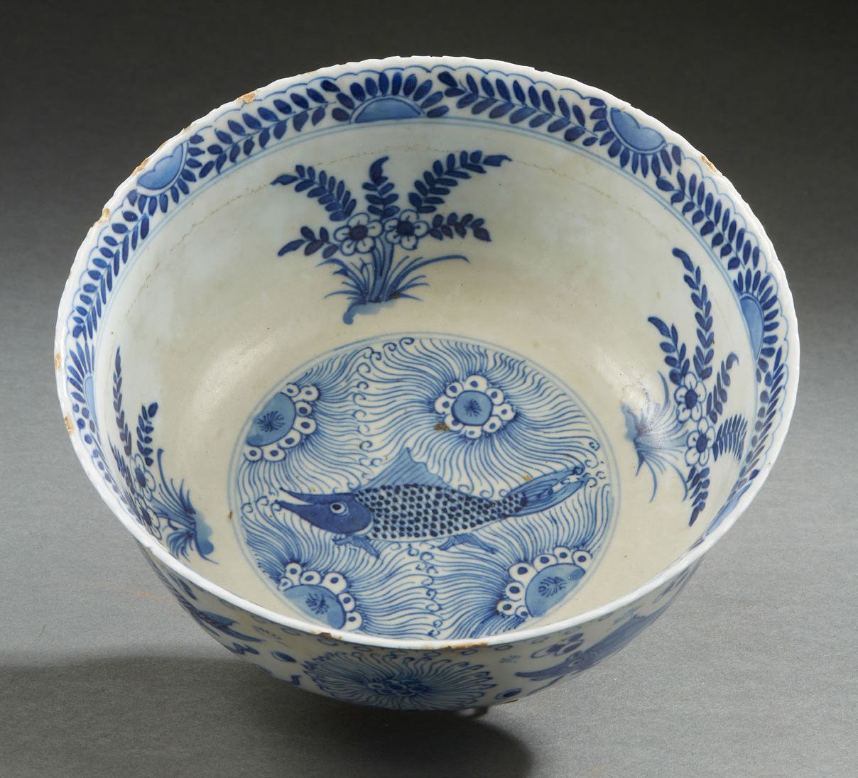 CHINE, XVIIIe siècle 青花瓷碗，装饰有鲤鱼和水生植物，中间的图案是盛开的花朵，反面则是内壁装饰的花束。
底部有康熙款。(边缘上的碎片)
H.&hellip;