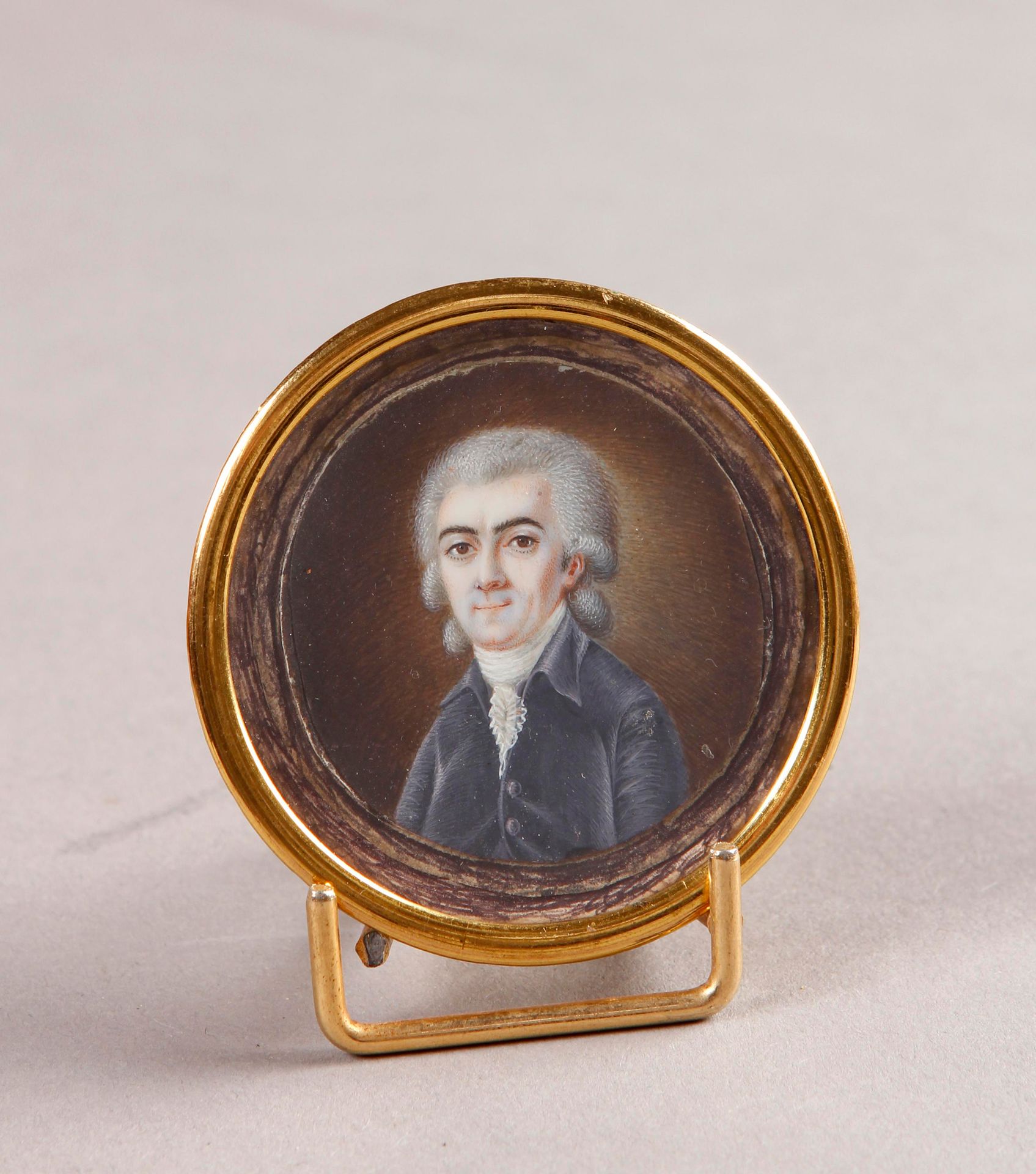 Null 约1790年的法国学校

穿着蓝色西装、戴着短假发、涂着粉的男子的画像

圆形象牙上的微型画。镀金的金属边框。

直径：5厘米