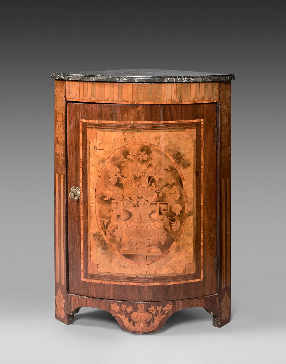Null 一个单门的弧形单板餐具柜，上面镶嵌着一个开花的瓮的装饰，在一个奖章中。立柱上装饰有花朵和模拟的凹槽。黑色脉络的大理石面板。

19世纪初的荷兰作品。
&hellip;