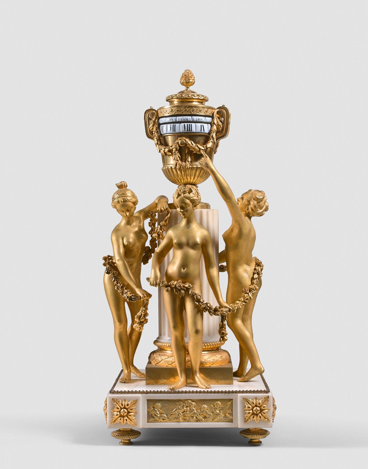 Null 鎏金青铜和白色大理石时钟，以Falconet的风格装饰，三个圣女围绕着一个柱子，支持一个带有旋转表盘的骨灰盒。螺旋式摆锤。底座上有高浮雕的爱情、交错和&hellip;