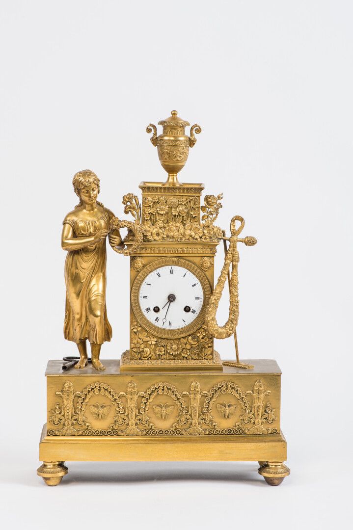 Null 一座带凹槽和镀金的青铜钟，表盘形成一个终端，白色珐琅的罗马数字，上面是一个有盖的花瓶，框架是一个年轻女子，手持花环和园艺主题的属性，在一个长方形的底座&hellip;