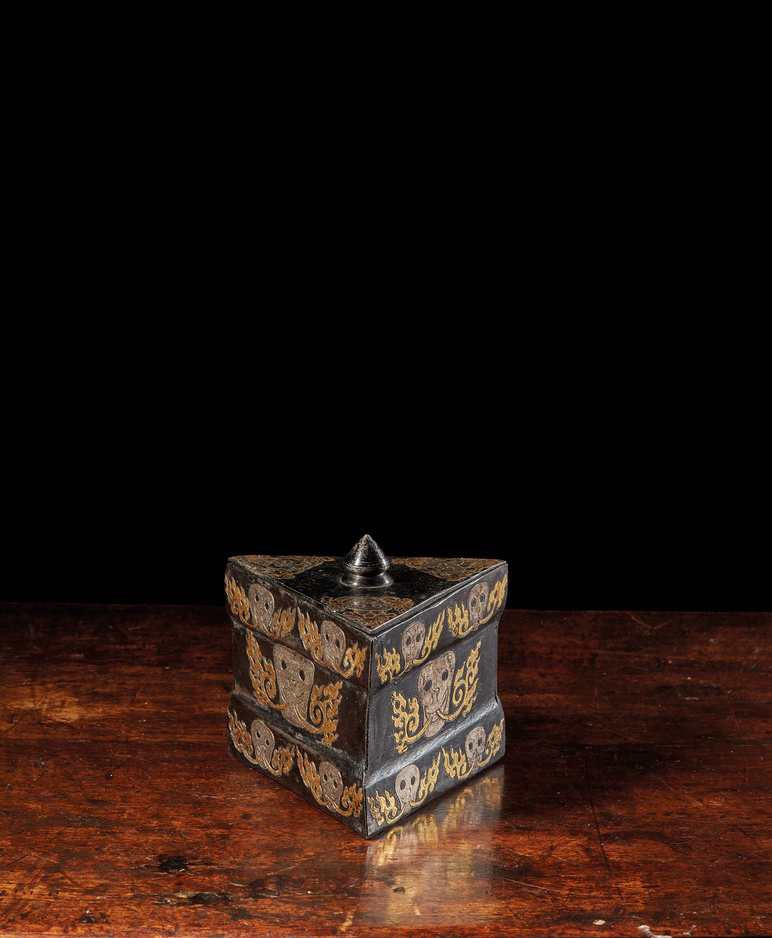 TIBET - XVIIe siècle 三角形铁盒，上面有金银铁合金装饰的风格化骷髅头，火焰从他们的嘴里喷出。
高8.3厘米，宽11.2
参考资料：类似的作品&hellip;