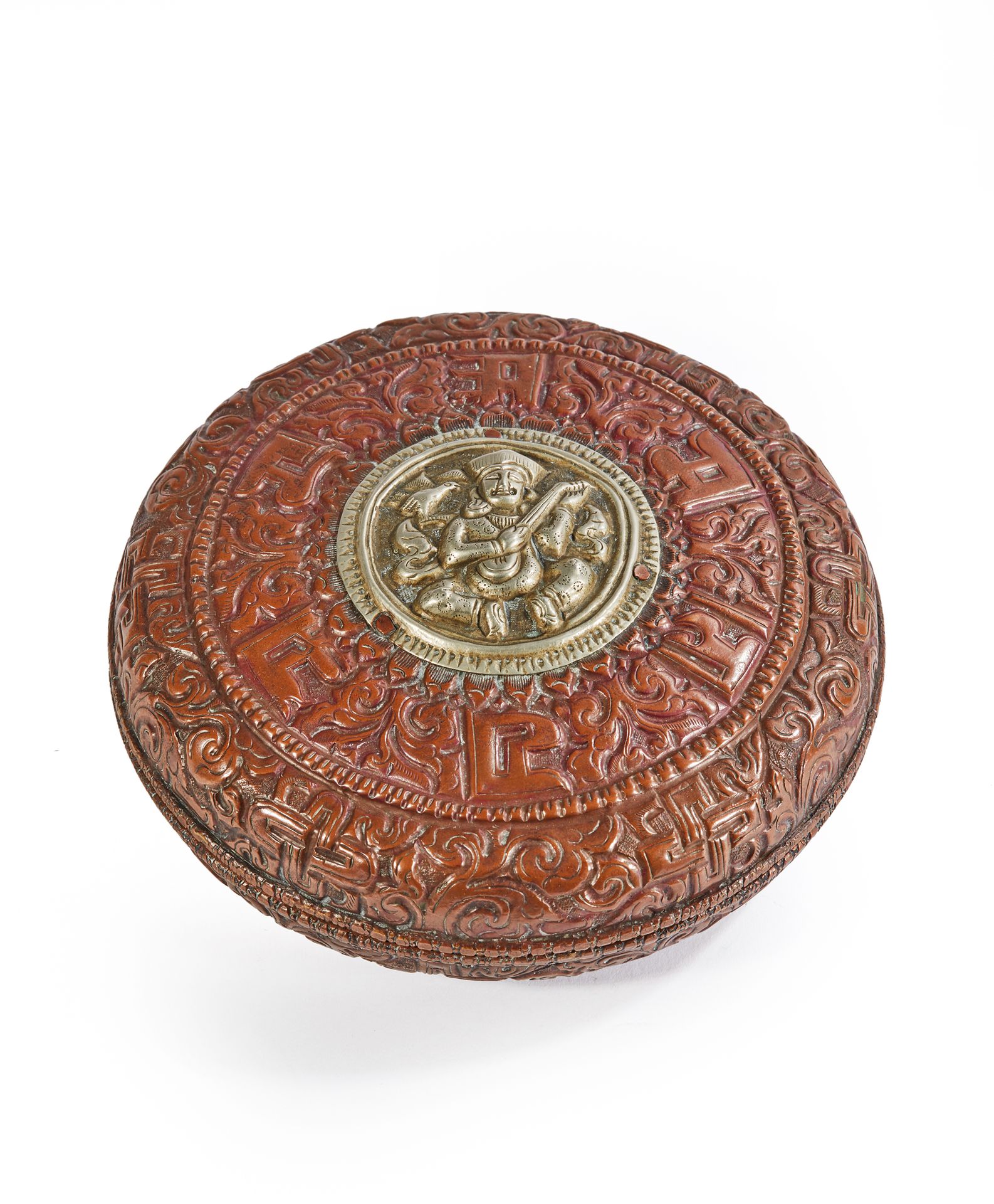 TIBET OU BHUTAN - XIXe siècle 一个圆形的铜盒，上面压印着花的卷轴和咒语，围绕着一个银盘，上面压印着一个弹琴的人物。
直径13厘米