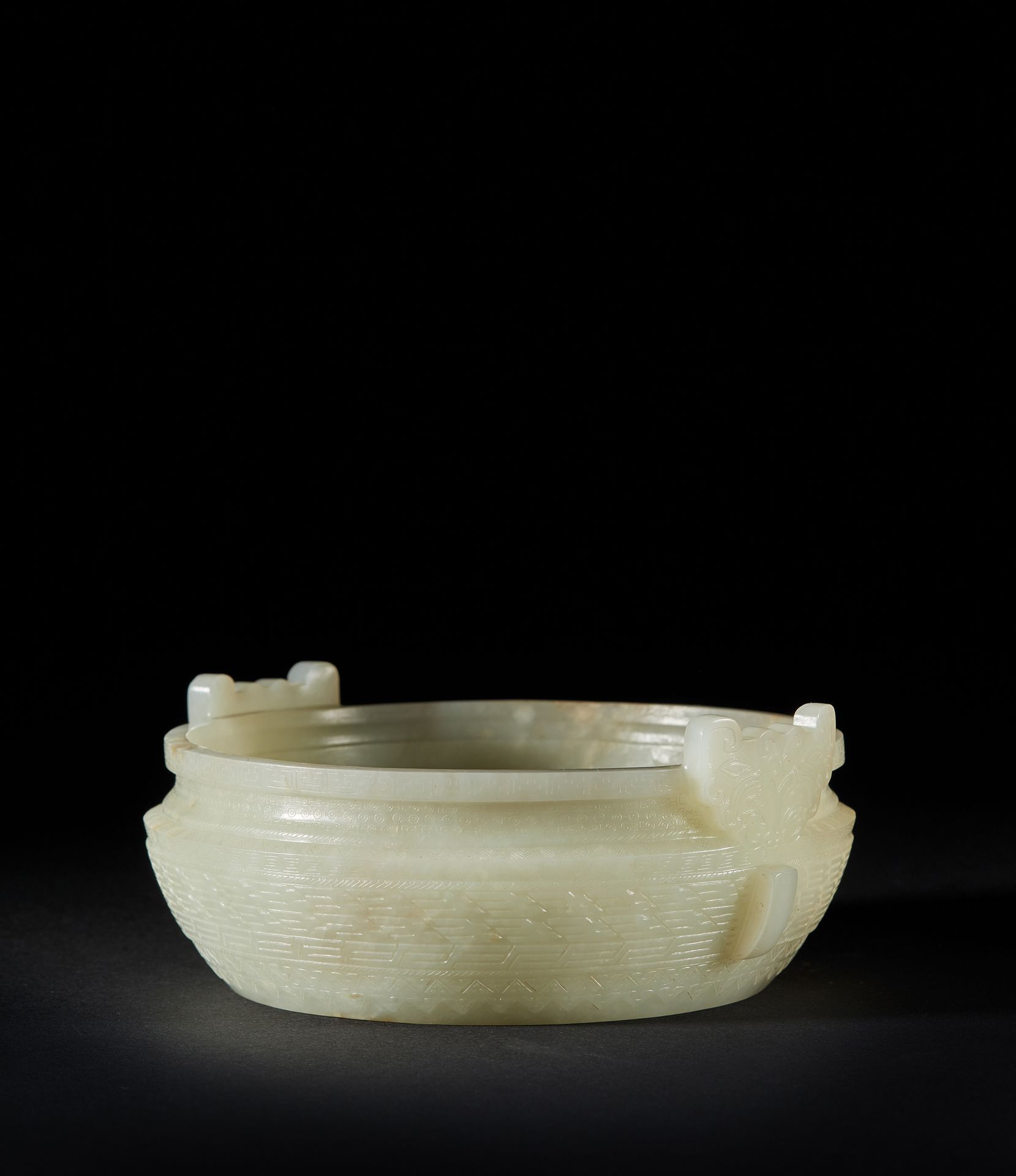 CHINE - XIXe siècle 一个圆形的青瓷玉碗，上面刻有几何图案，周围有雷纹和古代的纹饰。两个把手是饕餮面具的形式。
直径14.5厘米。高：无柄5.&hellip;