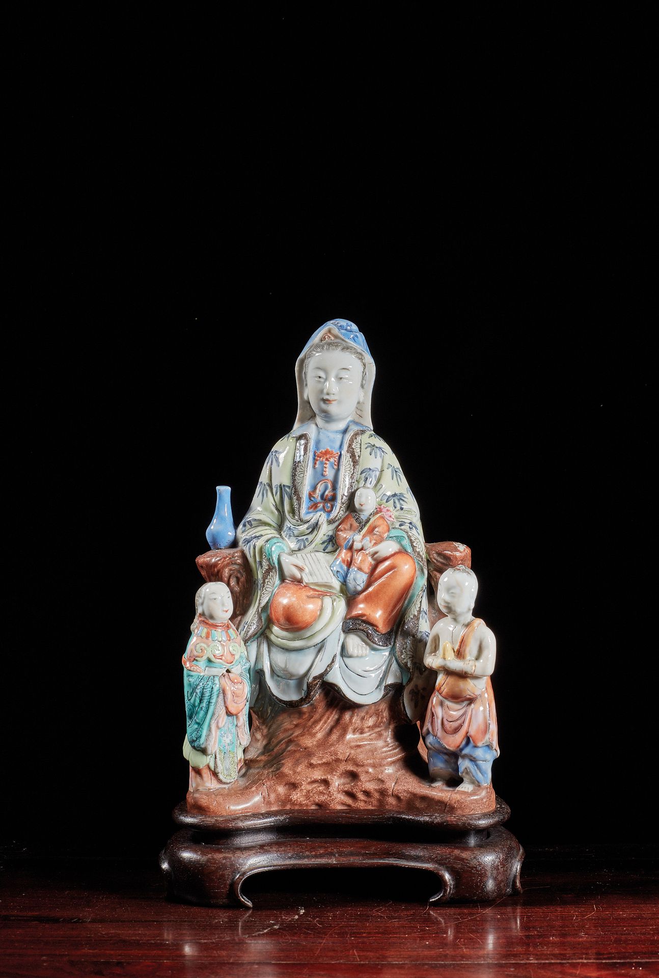 CHINE - XIXe siècle 多色珐琅彩观音像，坐在岩石上，抱着孩子和书，身穿黄底竹子装饰的袈裟，身边有龙女和善才。
H.22厘米。
木质底座