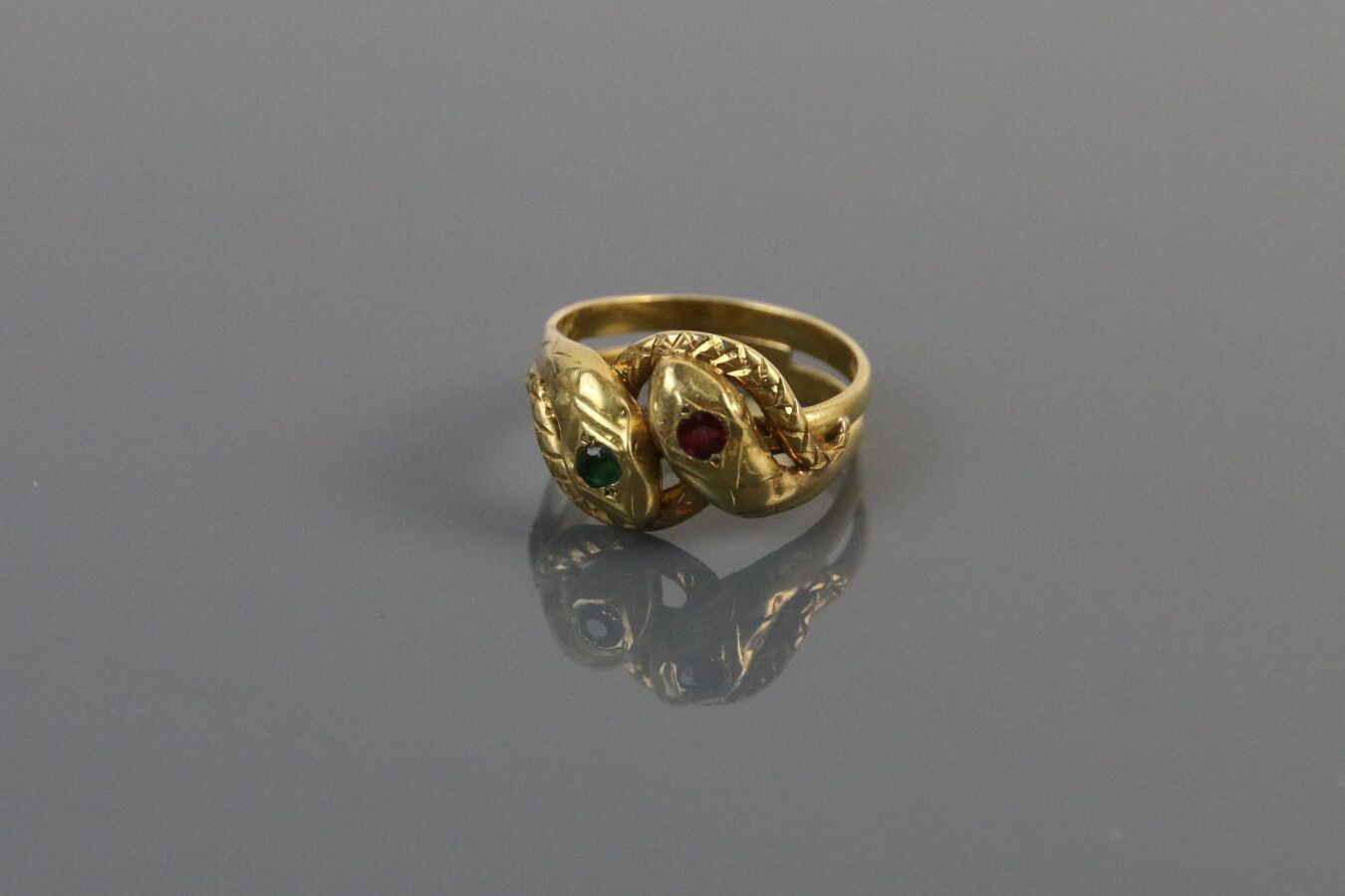 Null 750°/°的黄金戒指，部分镂空和雕刻，代表一条盘旋的蛇，镶嵌着一颗红色和一颗绿色的宝石。

TDD : 58 - 毛重 : 7,9 g
