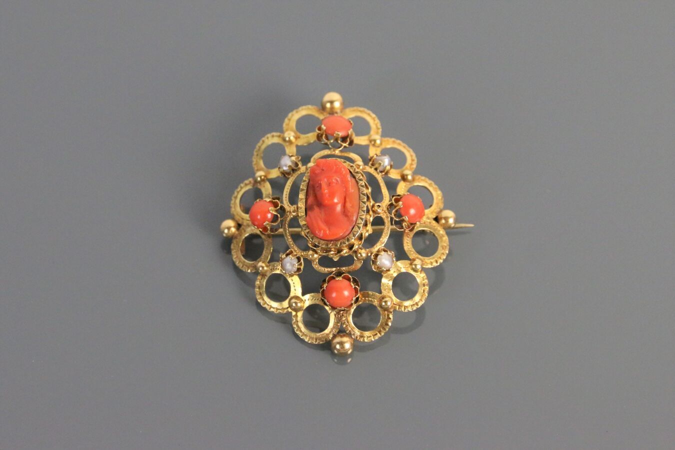 Null 750°/°的黄金胸针，有圆形的丝线装饰，饰有凸圆形珊瑚和珍珠，中心有一个代表女人的珊瑚浮雕。

19世纪的法国作品。

尺寸：4,2 cm - 毛重&hellip;