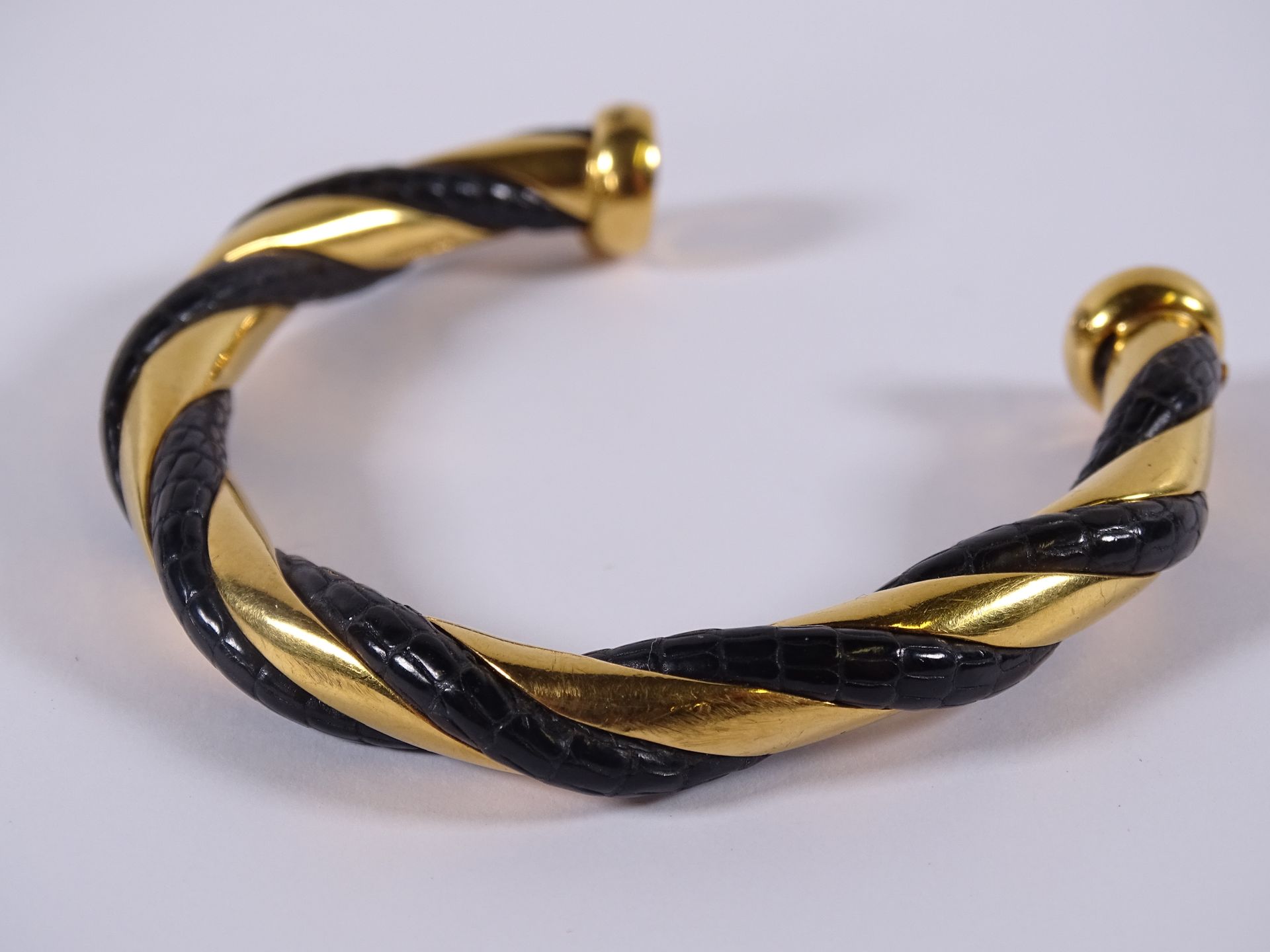 HERMES Bracelet jonc ouvert en métal doré à décor torsadé de cuir croco noir.

S&hellip;