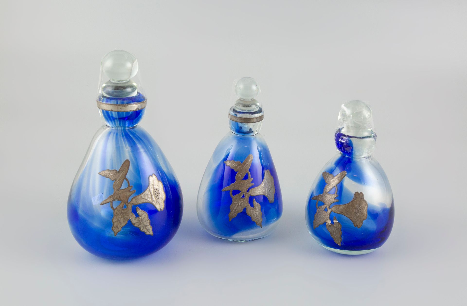 Null 让-克劳德-诺瓦罗（1943-2015）。三套蓝色有色玻璃瓶，装饰有锡器图案。(1个瓶塞损坏，1个瓶子上的锡叶脱落）。)
