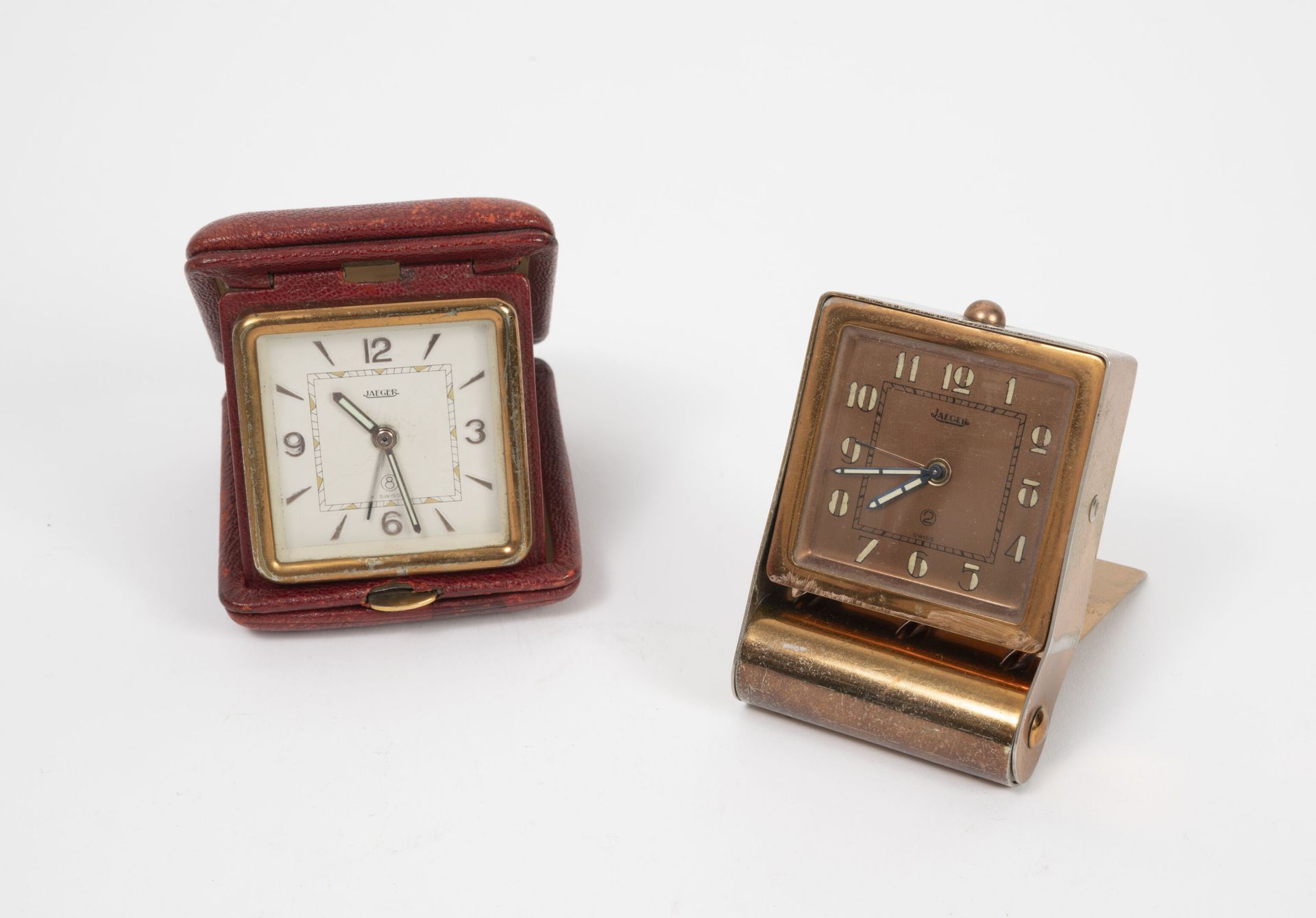 JAEGER LECOULTRE 两个镀金和镀铜金属的旅行钟。

- 一个是白色珐琅表盘，阿拉伯数字和时标。

机械机芯，手动上链。

装在一个红色的皮箱里。
&hellip;