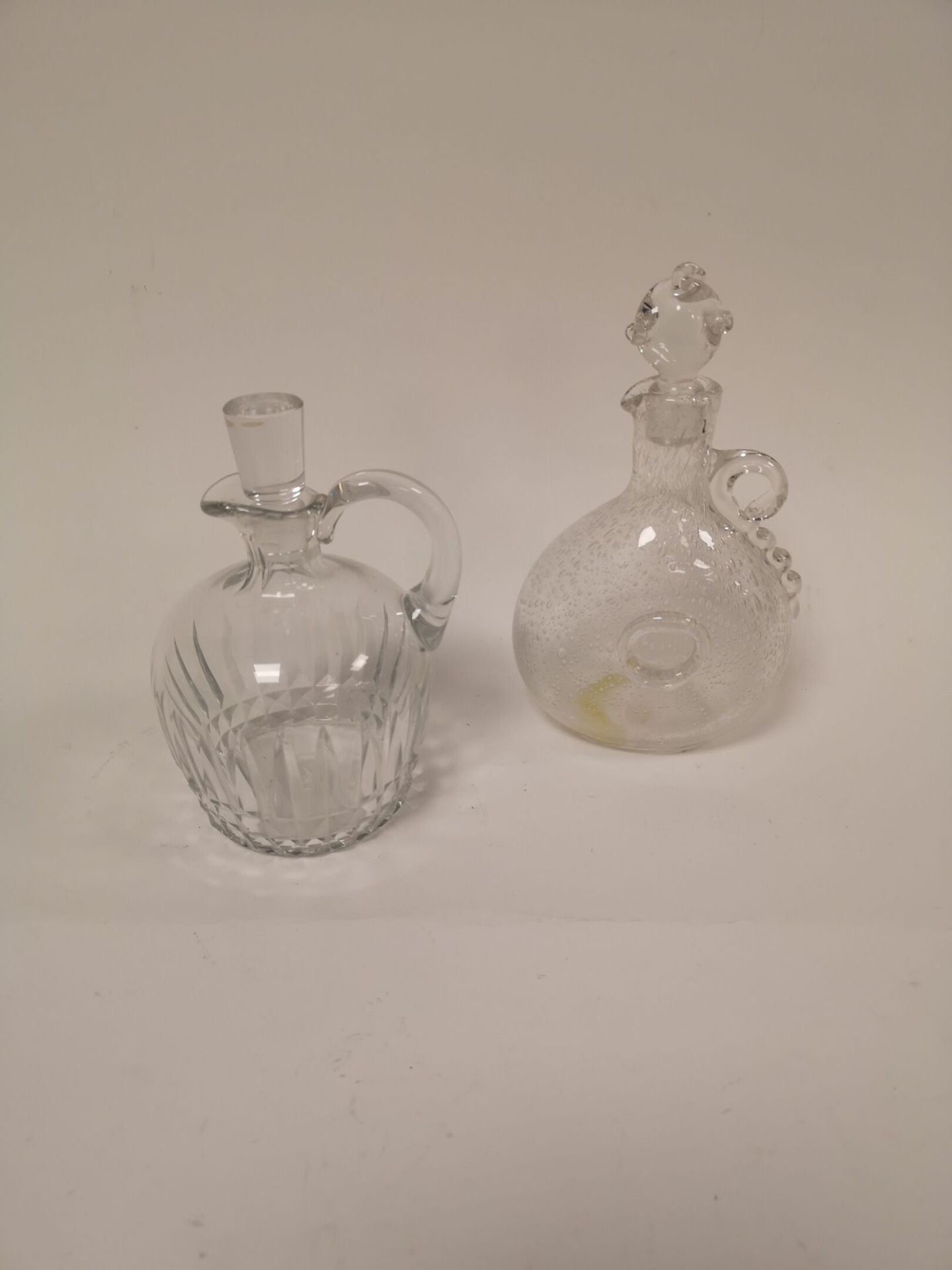 Null 两个无色玻璃酒壶:

- 一个由穆拉诺泡制的，带有奖章和热贴的手柄。

自由形式的塞子。

H.24.8厘米。 底部有黄色沉积物。

- 法航，切割方&hellip;