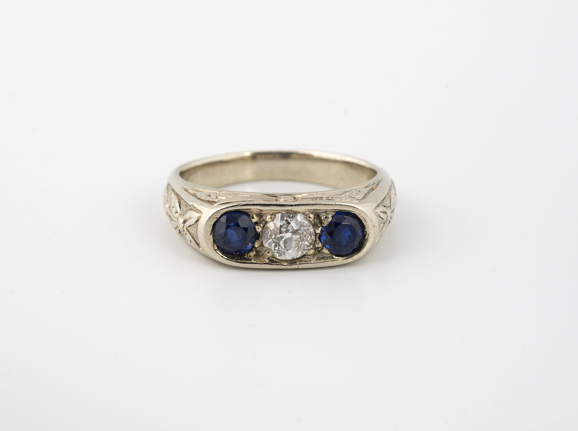 Null 一枚白金（750）戒指，椭圆形顶部交替镶嵌着两颗圆形刻面蓝宝石和一颗老式切割钻石，戒指上刻有树叶。

毛重：7.7克 - 手指大小：54。

刮伤和擦&hellip;