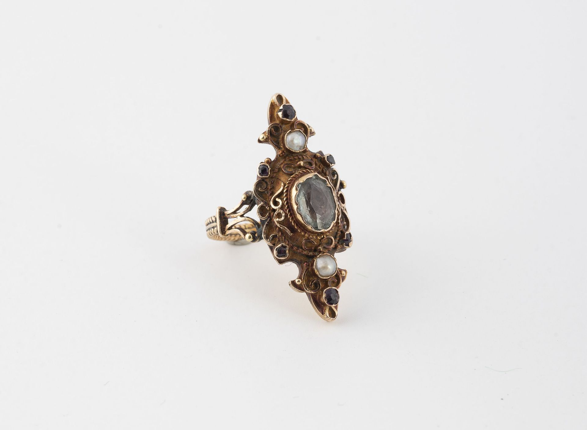 Null 玫瑰金(750)侯爵型花戒，中心镶嵌了一颗封闭式的椭圆形刻面海蓝宝石，周围有金丝卷轴、小型圆形刻面红宝石和两个封闭式的白色半宝石。
戒指上有编织的图案&hellip;
