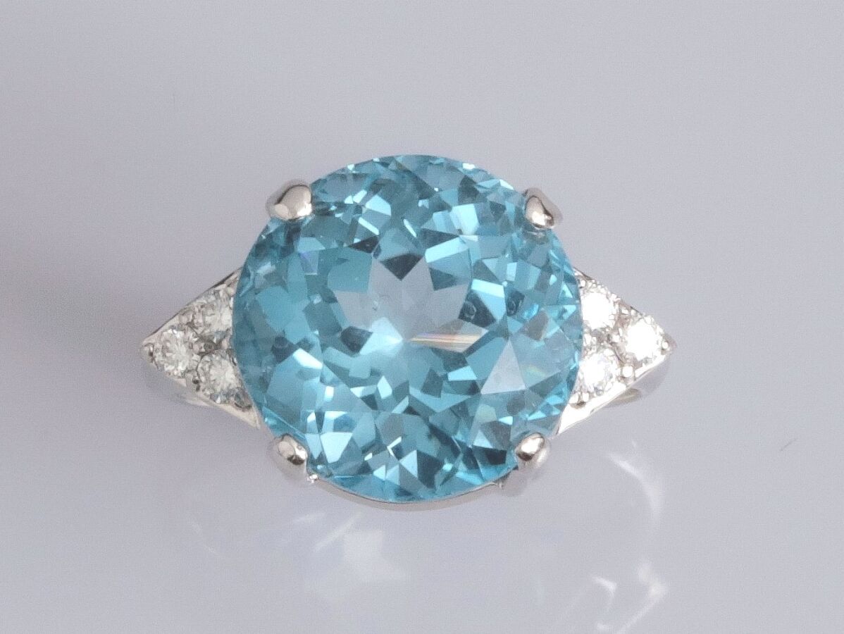 Null 18K白金戒指，镶有一颗约12克拉的圆形蓝色托帕石，两侧各有三颗明亮式切割钻石，重7.6克。TDD 53.宽度：12.6毫米。标有一个鹰头。