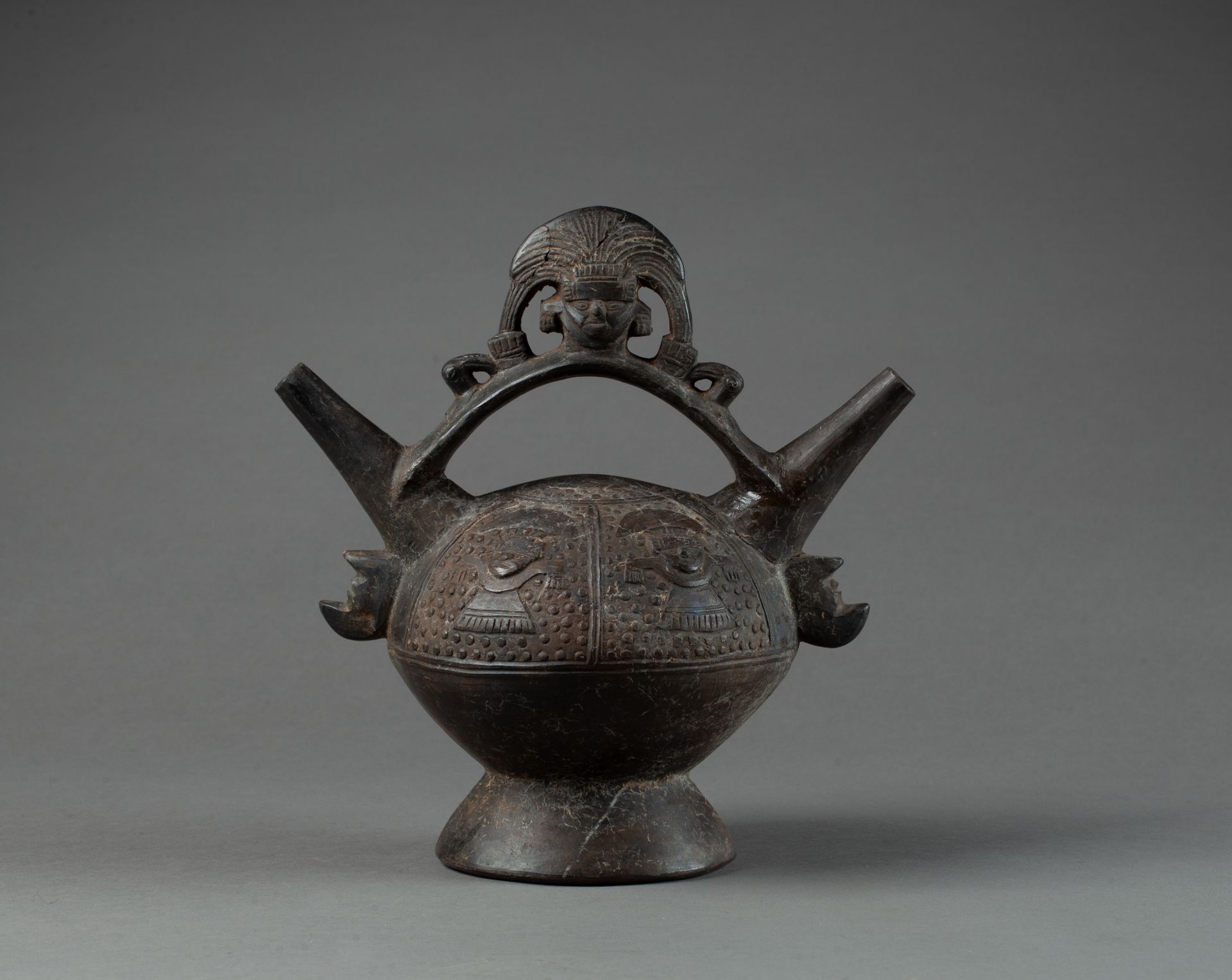 Vase étrier 饰有带扇形头饰的神灵头像。身体上显示出四个祭司，他们的手象征性地朝向大地。

棕色赤土。

秘鲁兰巴耶克，公元1100-1400年。

&hellip;