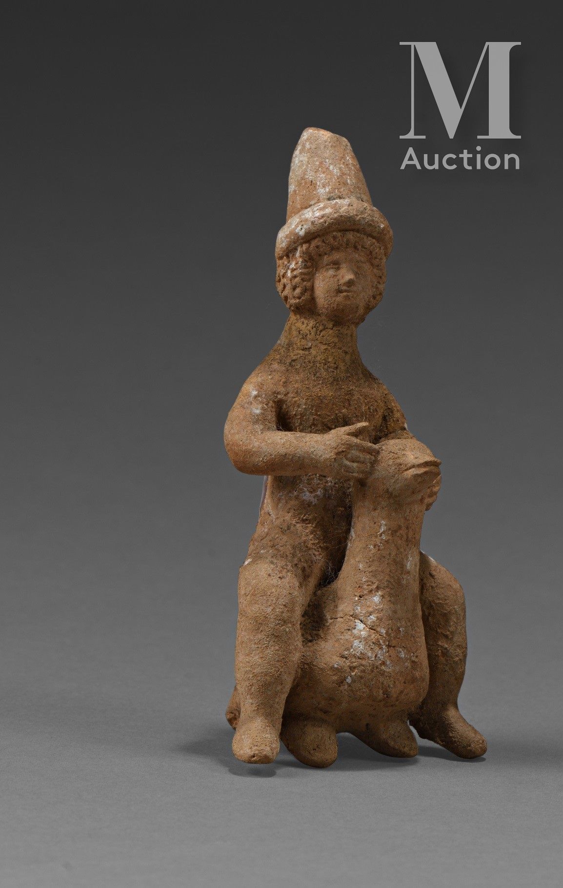 Figurine d’enfant nu, vêtu d’un haut bonnet. Il est assis sur un palmipède.

Ter&hellip;