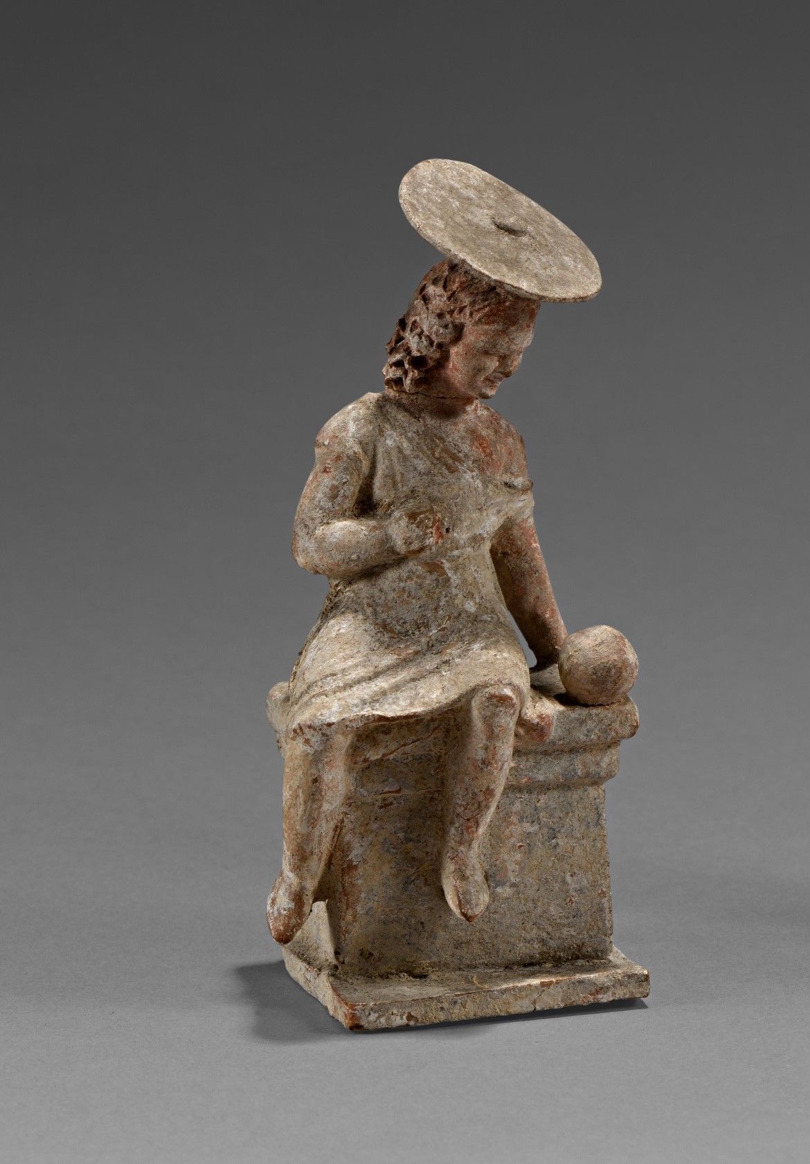 Figurine de jeune fille assise sur un autel. 她身穿短外衣，戴着一顶圆盘状的帽子。她似乎在看她面前的一个球。

赭色&hellip;