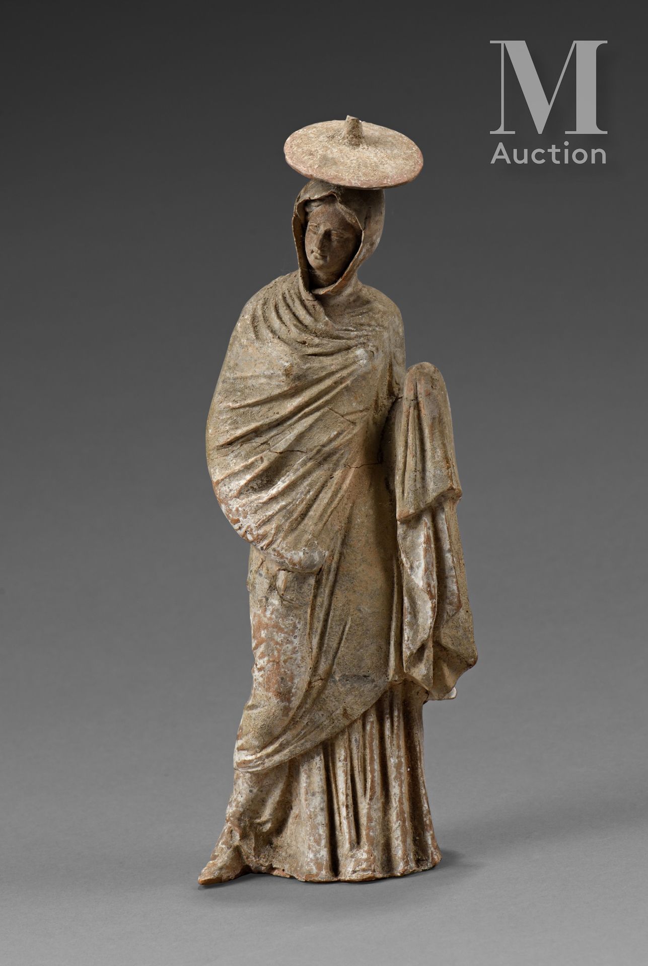Figurine péplophore, emmitouflée dans un long manteau. 一顶盘状的帽子被放在它的头罩上方。

赭石色赤土，&hellip;