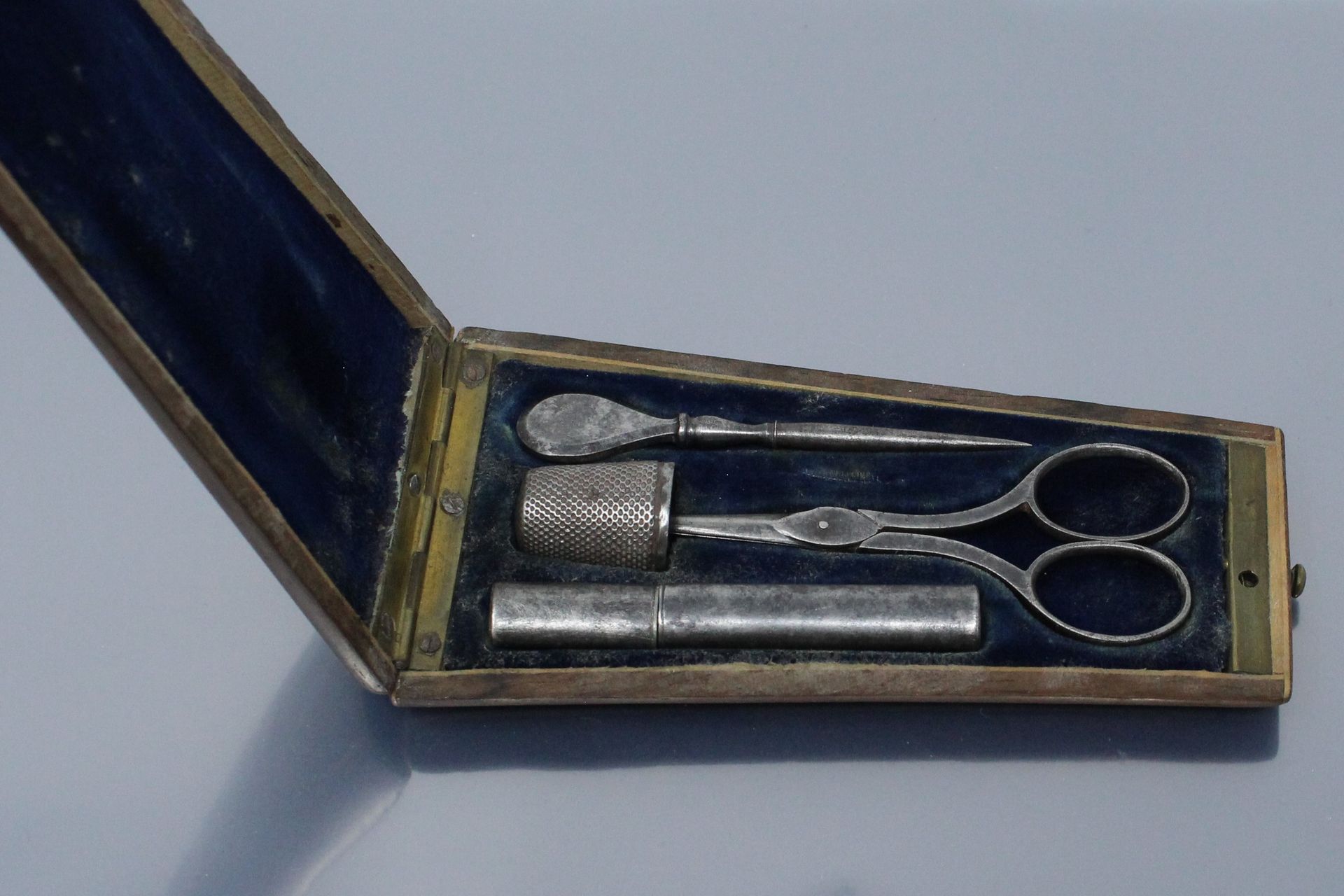 Null 金属缝纫套装装在一个红木和黄铜镶嵌的盒子里，它包含一把剪刀，一个打孔器，一个针盒和一个顶针。19世纪。

尺寸：12.5 x 7厘米。