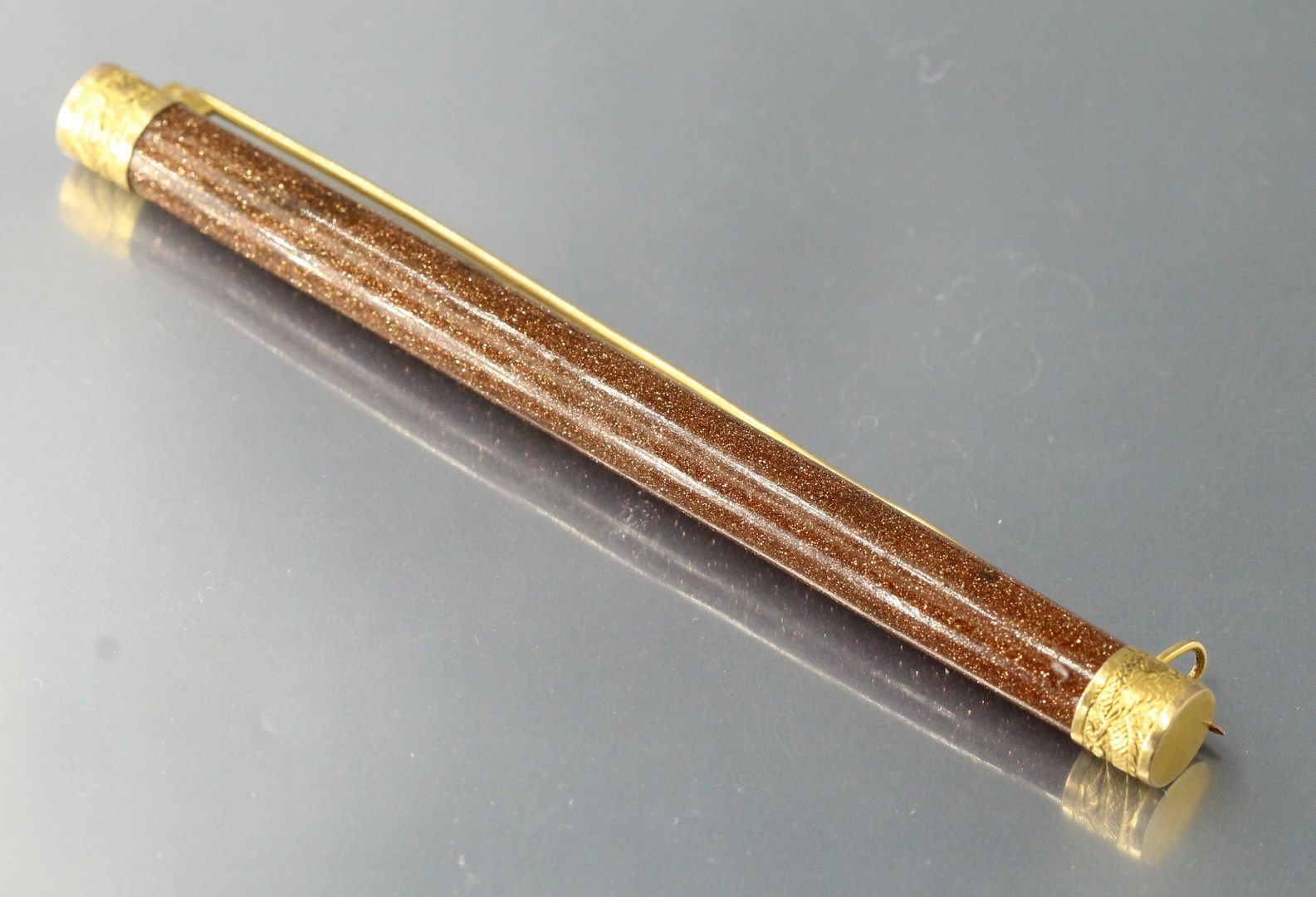 Null 圆柱形砂金石玻璃胸针，配以18K（750）金尖和针。

长度：9.3厘米。- 毛重：12.82克。