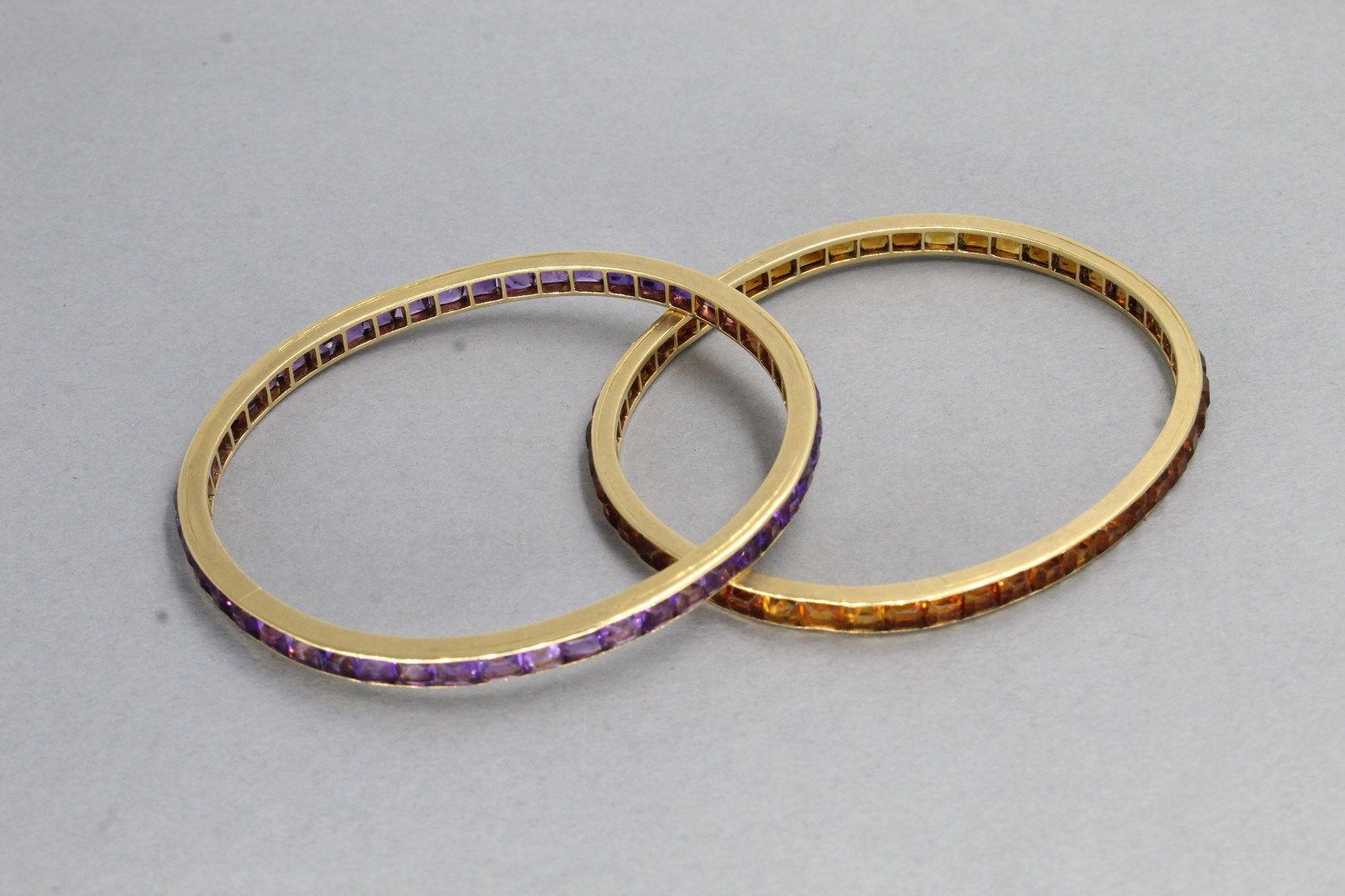 Null 一套两个椭圆形的18K（750）黄金手镯，一个镶有校准的黄水晶，另一个镶有校准的紫水晶。

内周长：约18厘米。 - 毛重：26.96克。